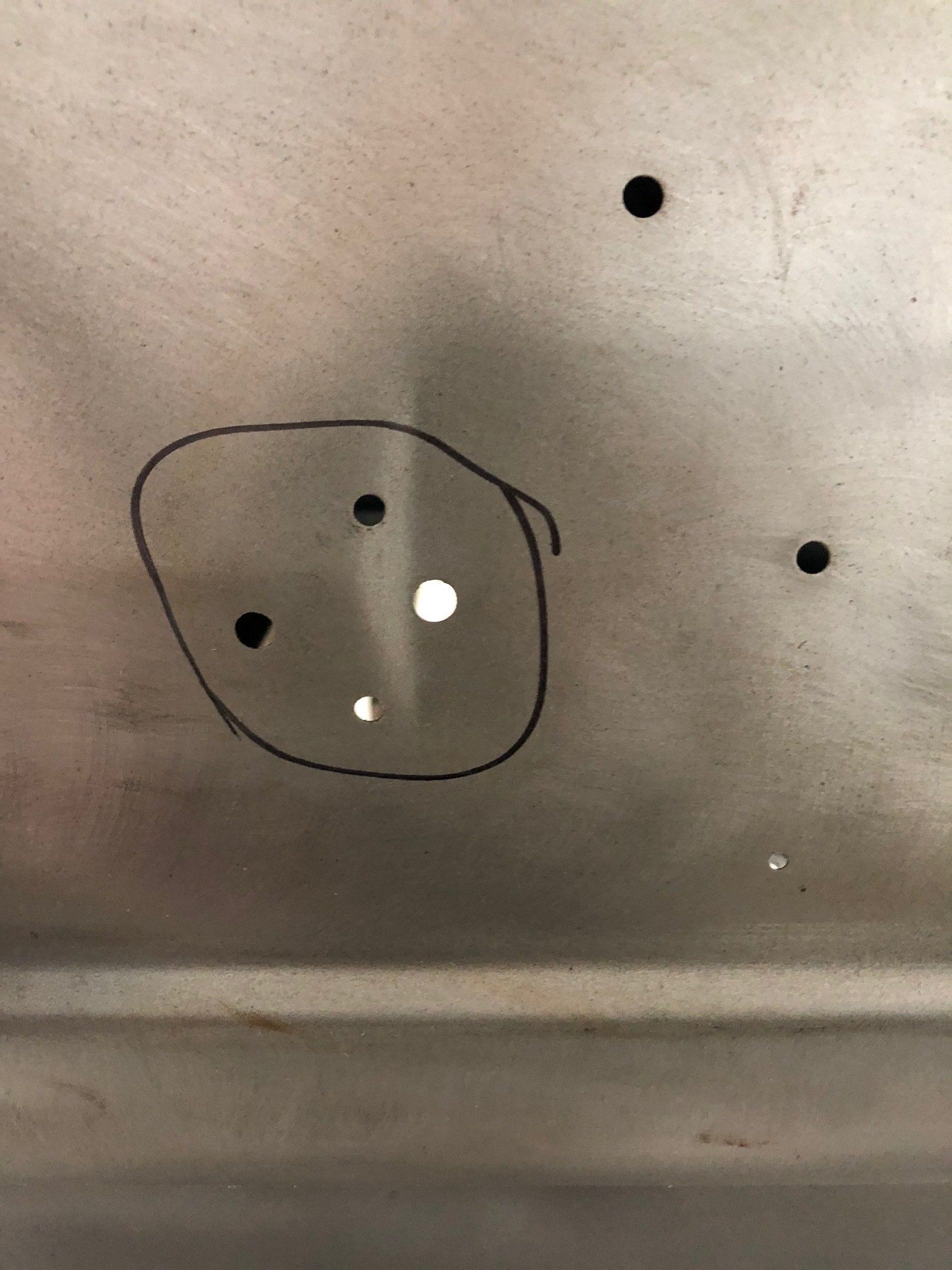 Circled small dark holes on a beige wall or panel, with a white spot nearby.