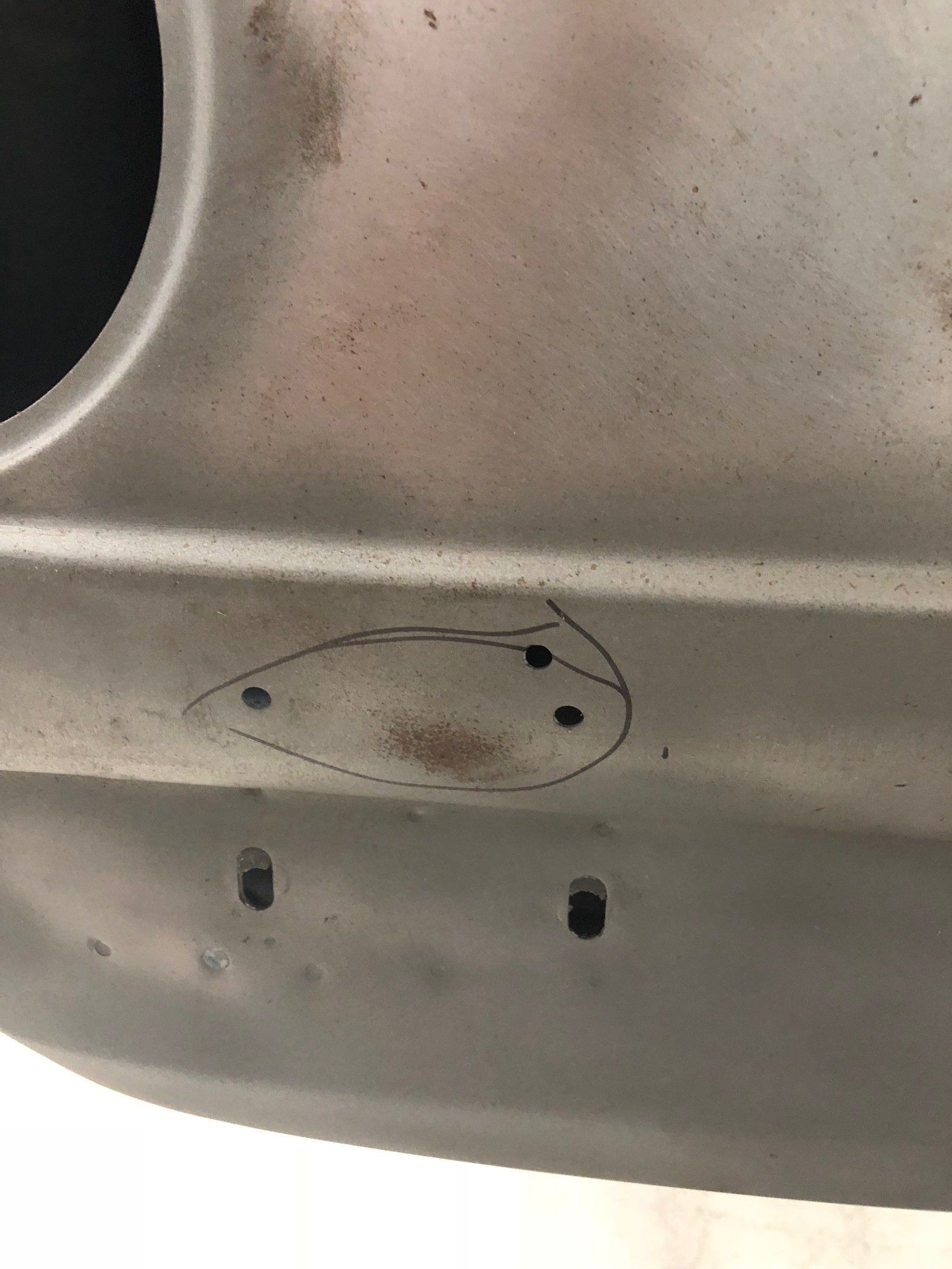 Close-up of a beige metal surface with two small dark holes and a black outlined oval marking.