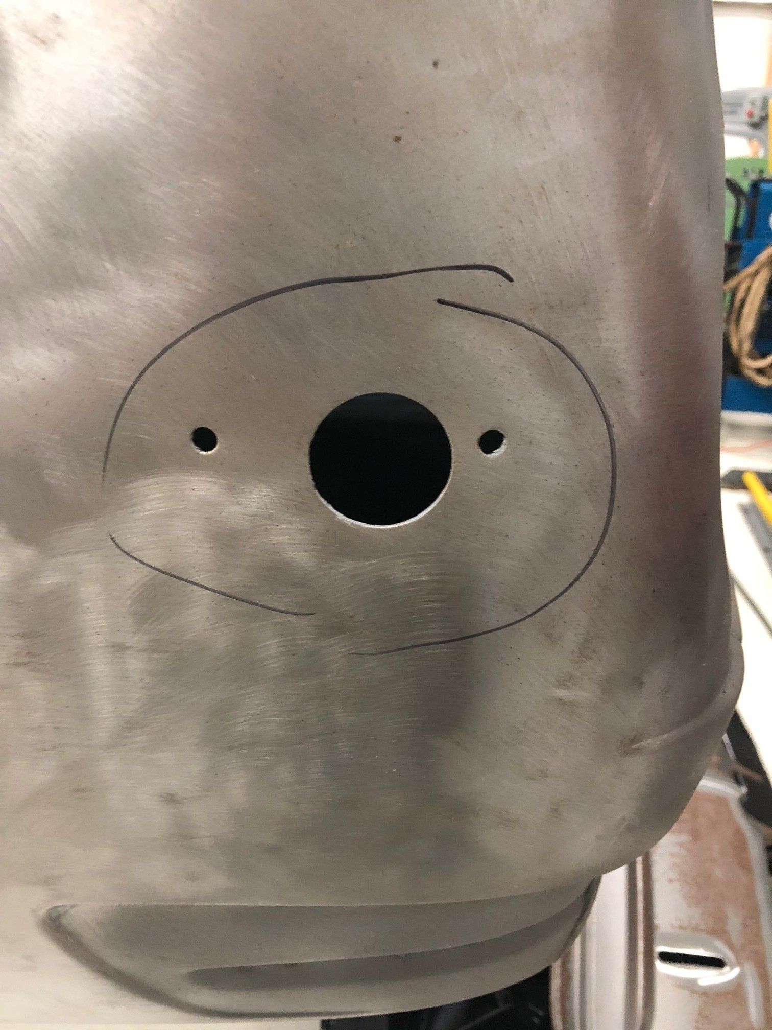 Gray metal panel with a hand-drawn face, black circular nose and eyes, and a curved mouth outline.