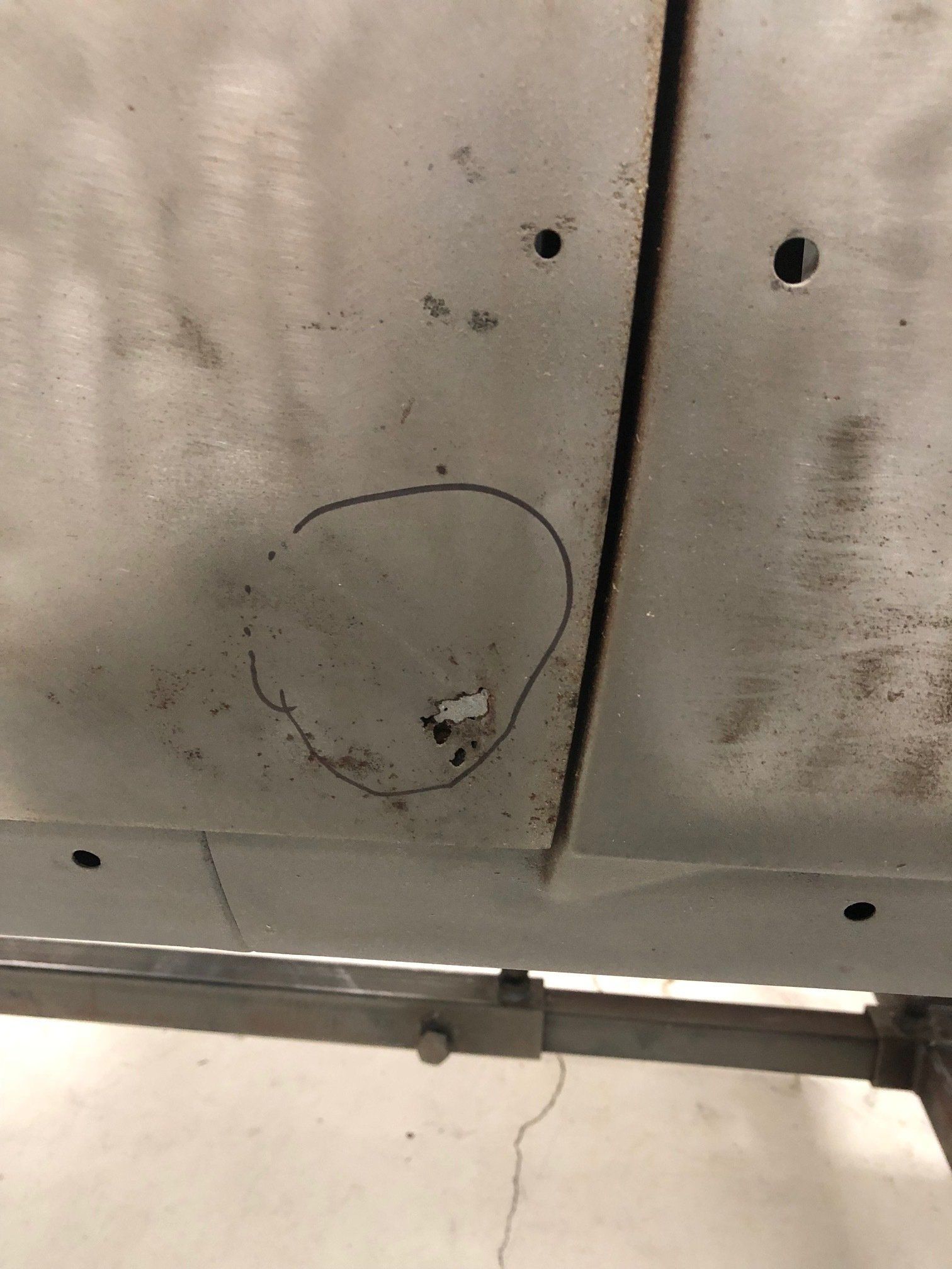 Close-up of a stained metal ceiling with a small circular mark, screws, and a crack near the bottom edge