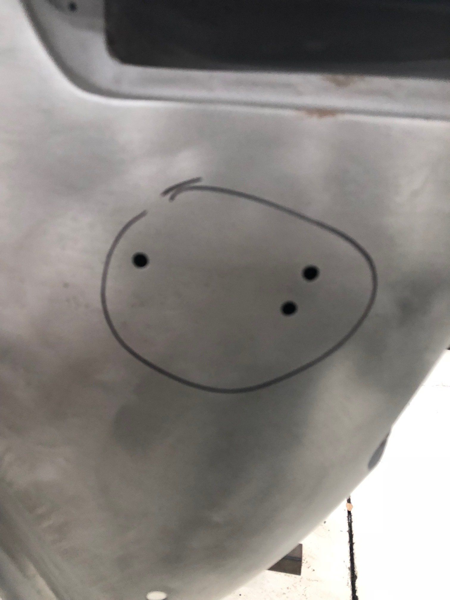Close-up of a gray surface with a simple black doodle face and a small curved line above it