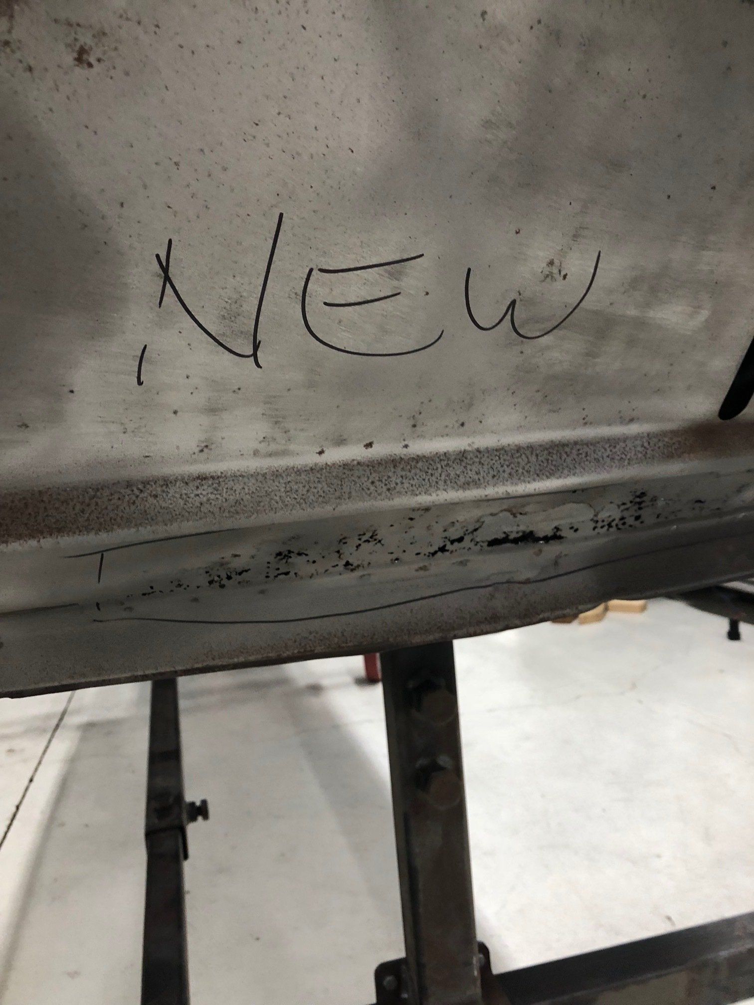 Handwritten “NEW” on a dirty gray metal surface with a dark stand below.