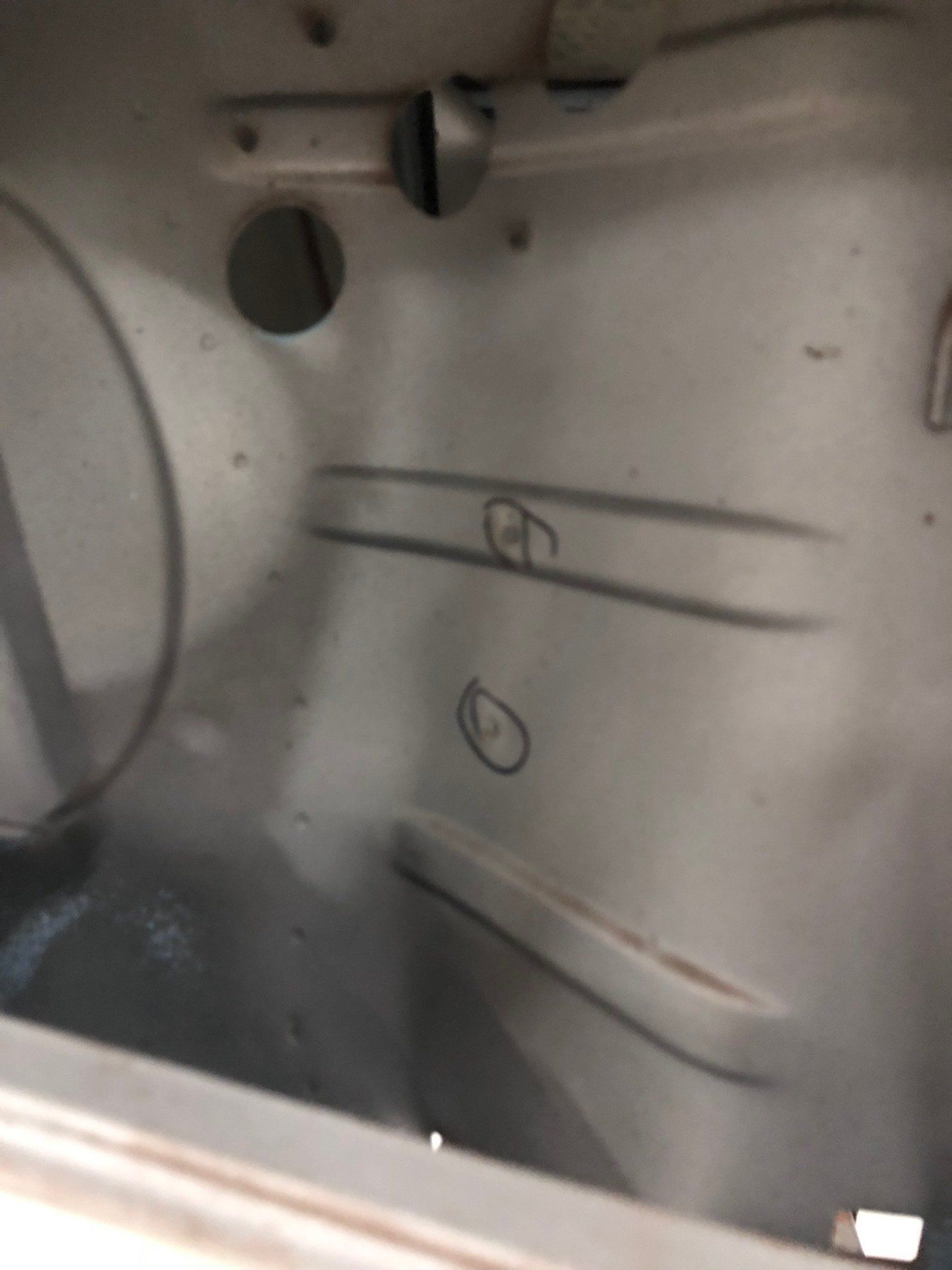 Close-up of a gray metal interior panel with circular holes and two hand-drawn markings.