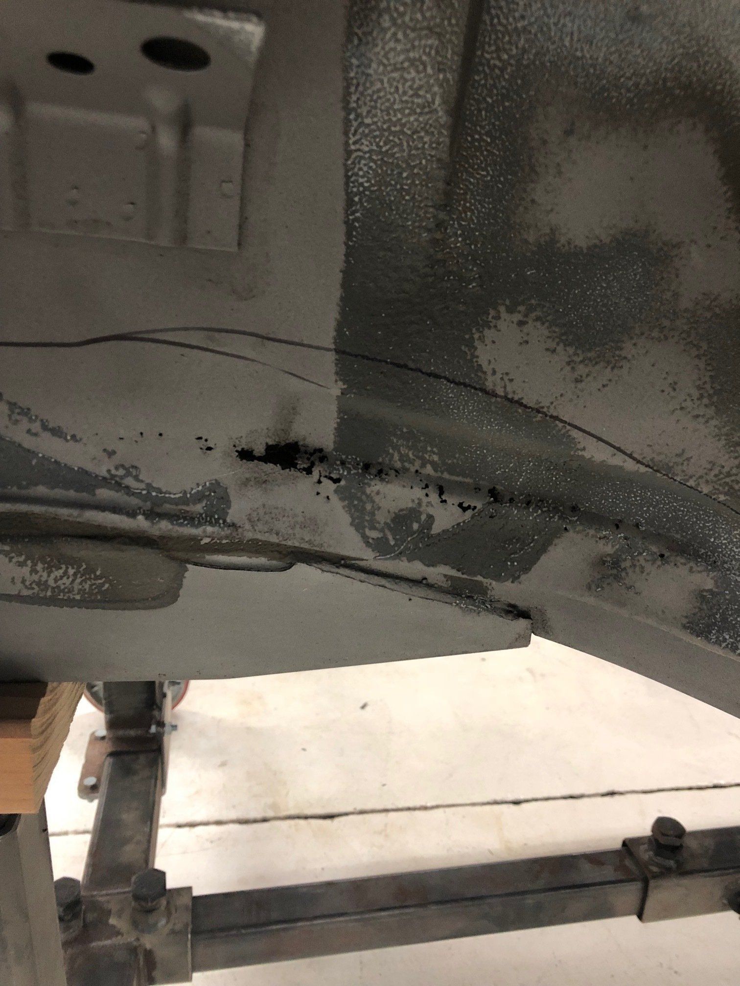 Close-up of a damaged gray vehicle underside with cracks and black scuffs near a metal support bar