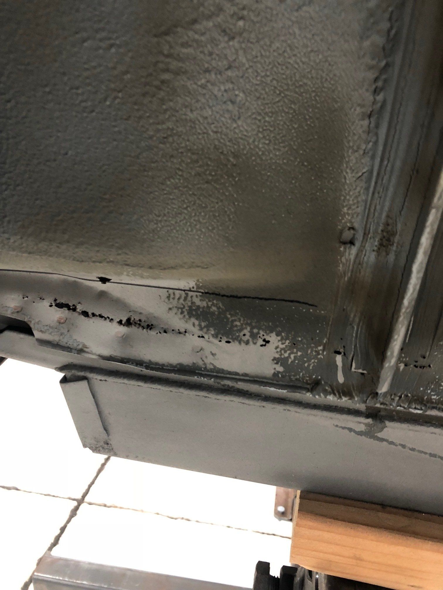 Close-up of a black metal panel with peeling paint and scuffed edges near a tiled floor.