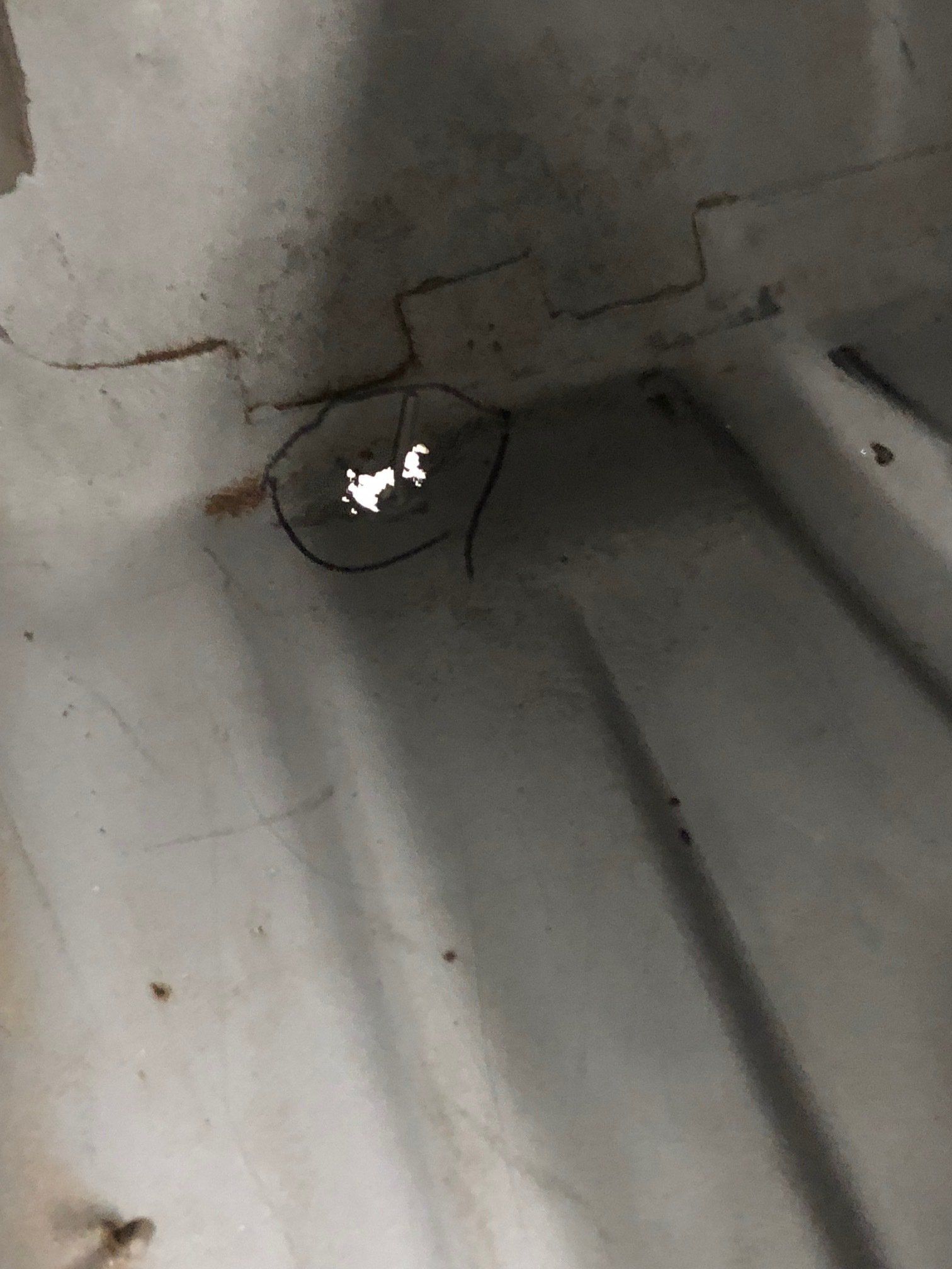 Small dark hole in a gray ceiling or wall, with a bright reflection inside and cracks around it