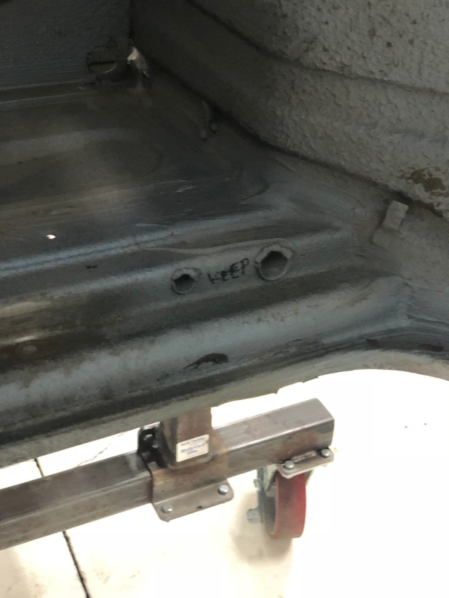 Close-up of a car seat mounting bracket and metal floor pan with a red lever underneath.