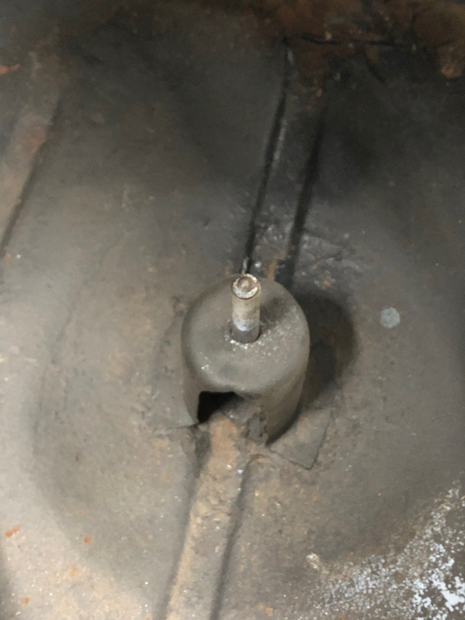 Close-up of a gray metal valve with a small bolt in a dusty circular basin.