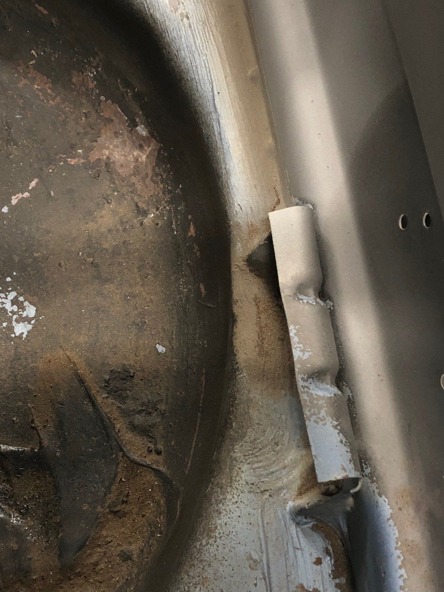 Close-up of a metal hinge on a worn, dirty surface with rust and peeling paint.