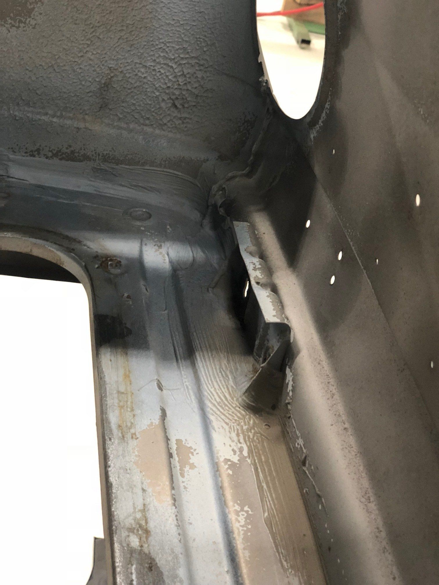 Close-up of a dark metal interior with a narrow rust-streaked seam and a small oval opening.