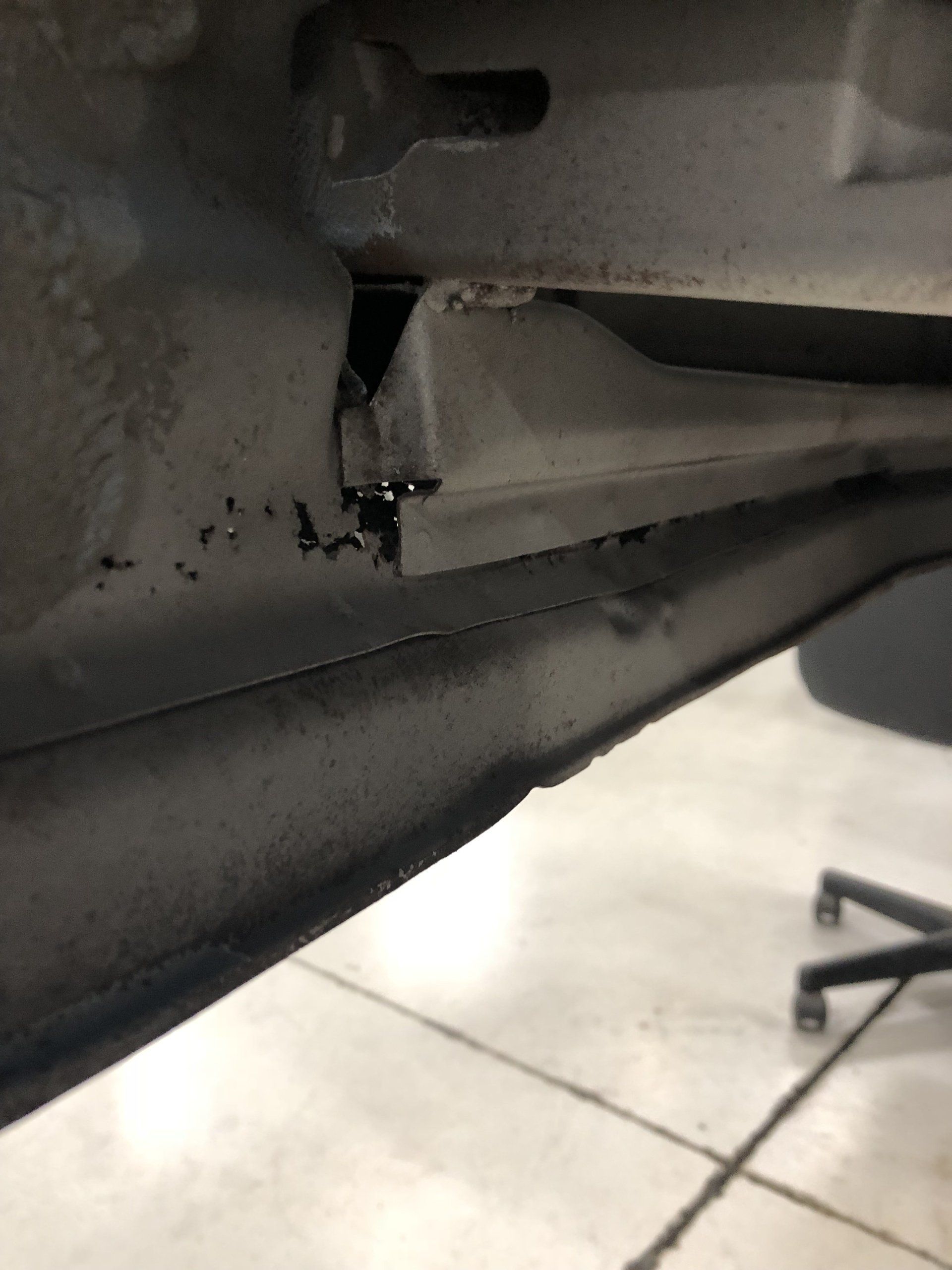 Close-up of a damaged black plastic panel with a broken bracket and debris on a tiled floor.