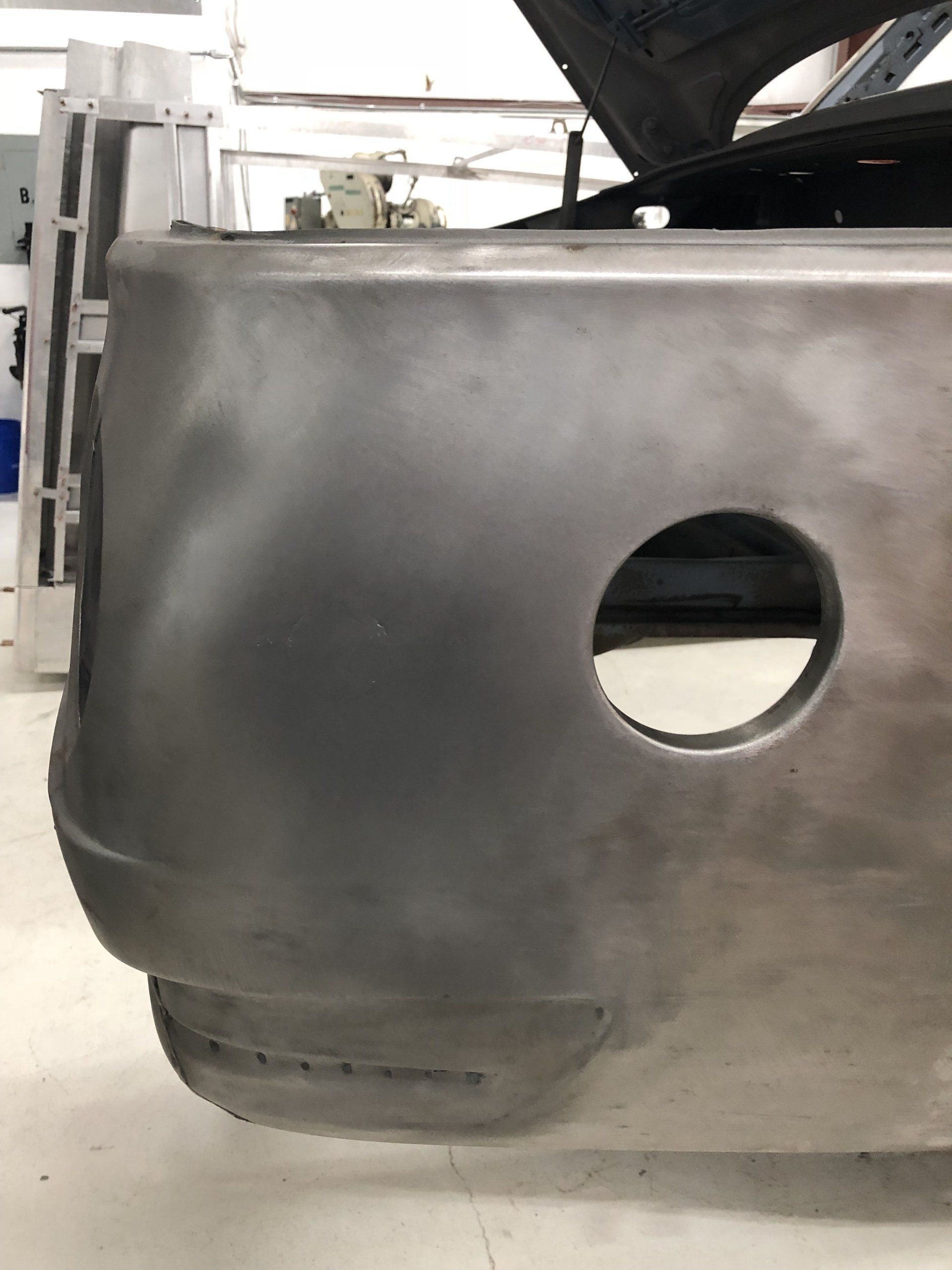 Gray car bumper panel with a round cutout in an automotive workshop