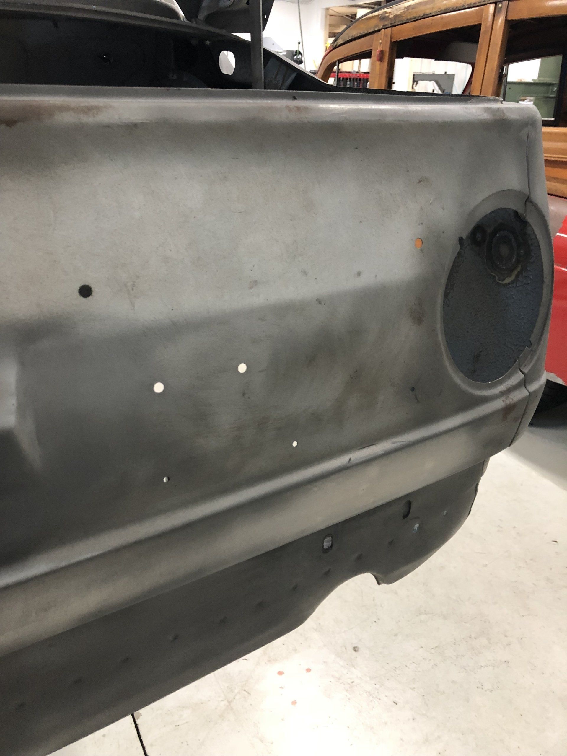 Gray car door panel with a round speaker opening and small holes in a workshop setting