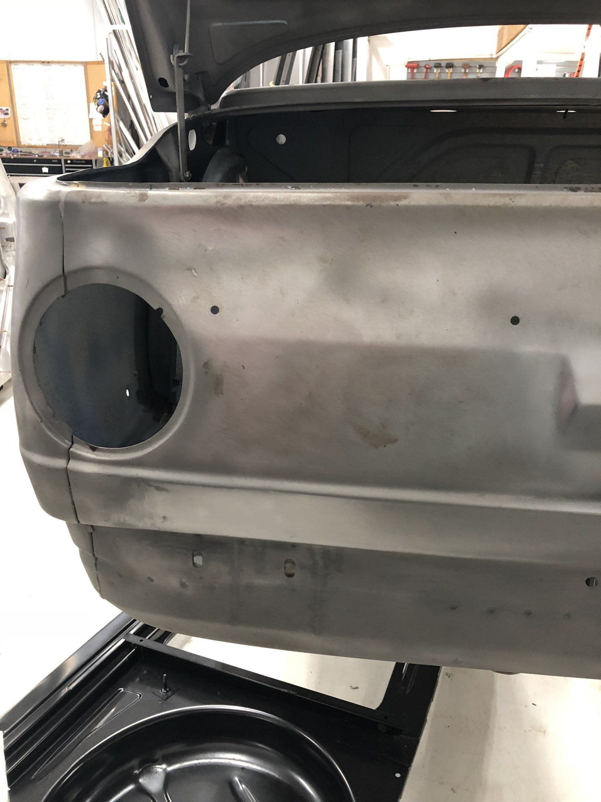 Primed car rear quarter panel with circular taillight opening in a workshop