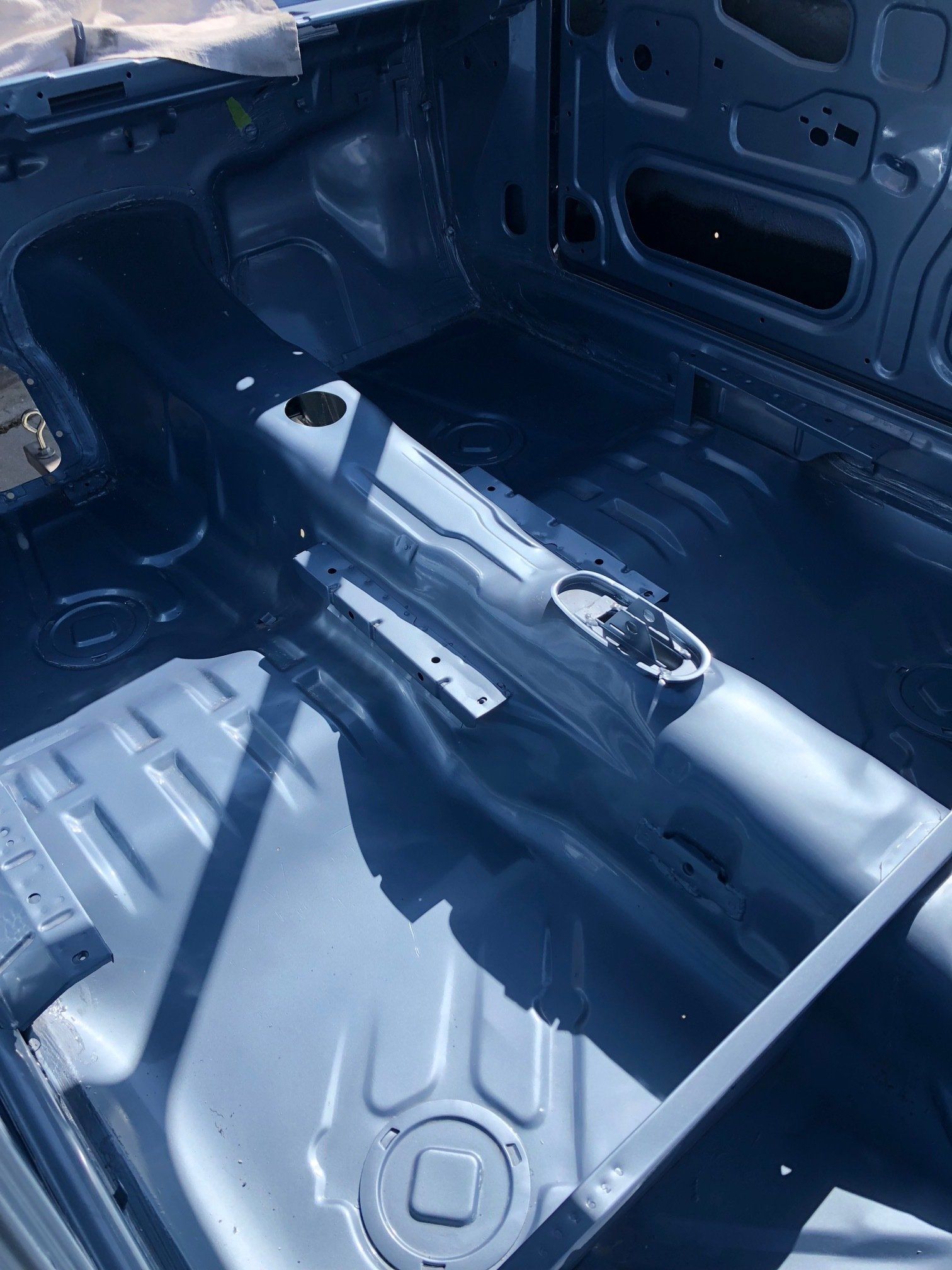 Empty car trunk interior with exposed metal floor in blue-gray primer
