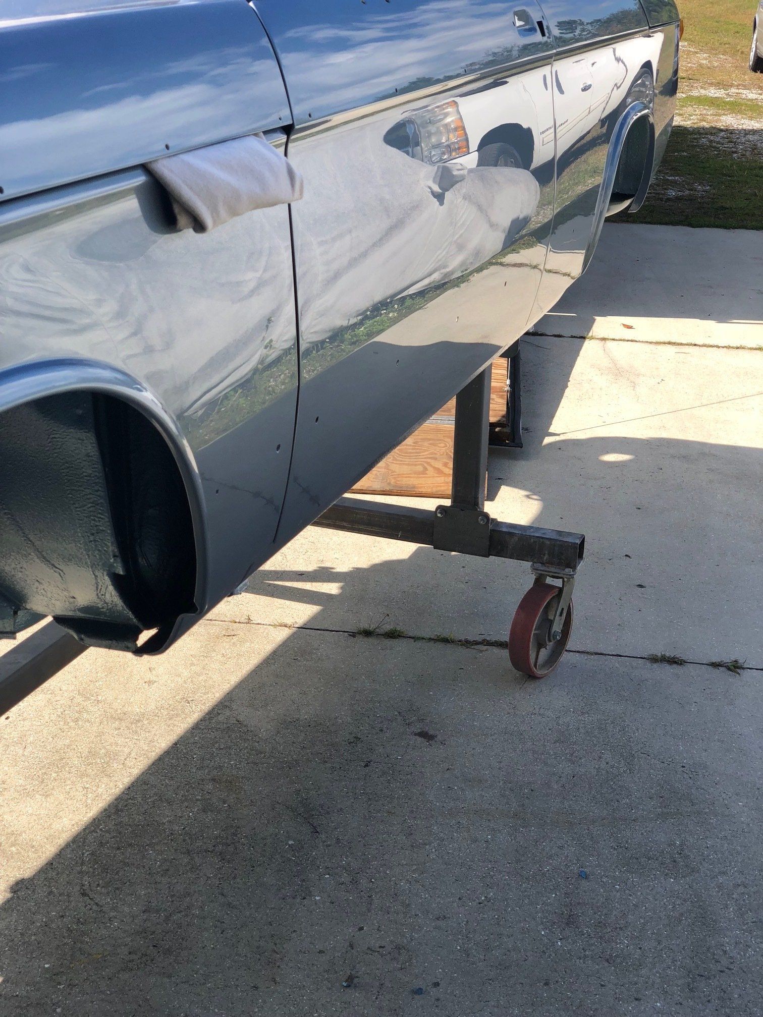Damaged blue car body on a jack stand in a driveway, with a dented side panel