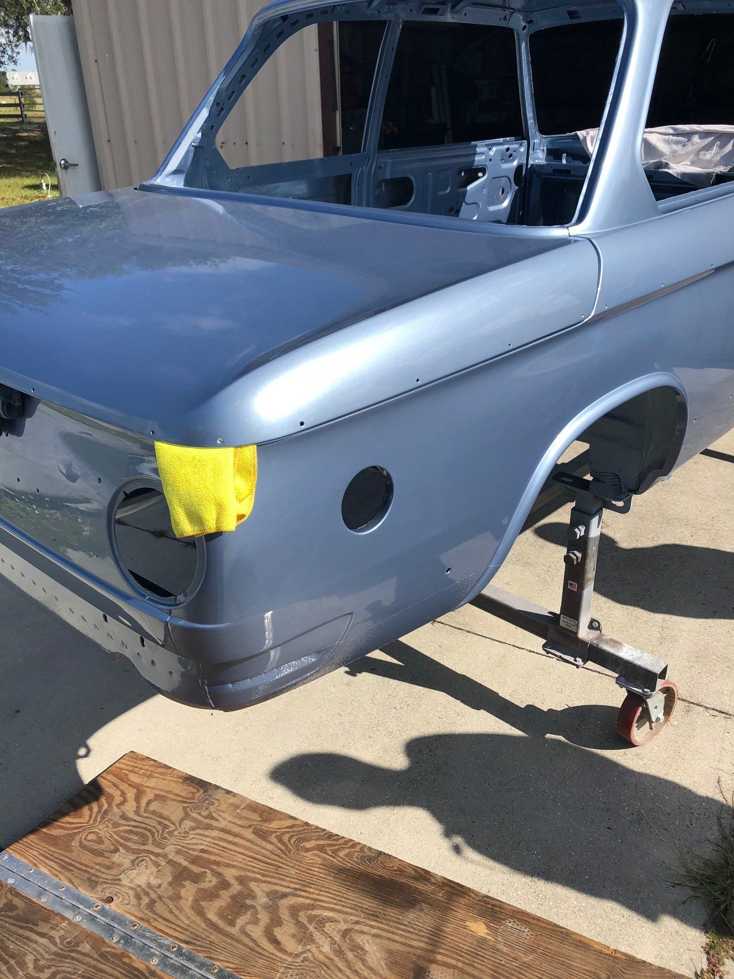 Gray classic car body on jack stands with yellow tape over the headlight area in a driveway