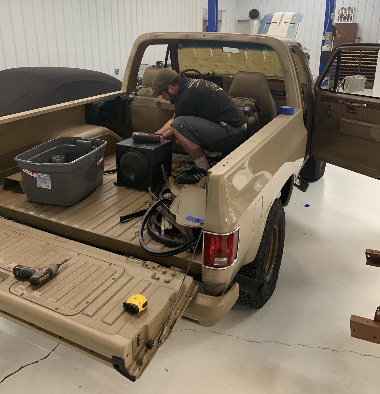Person working inside beige pickup truck bed in a garage, with tools and equipment nearby