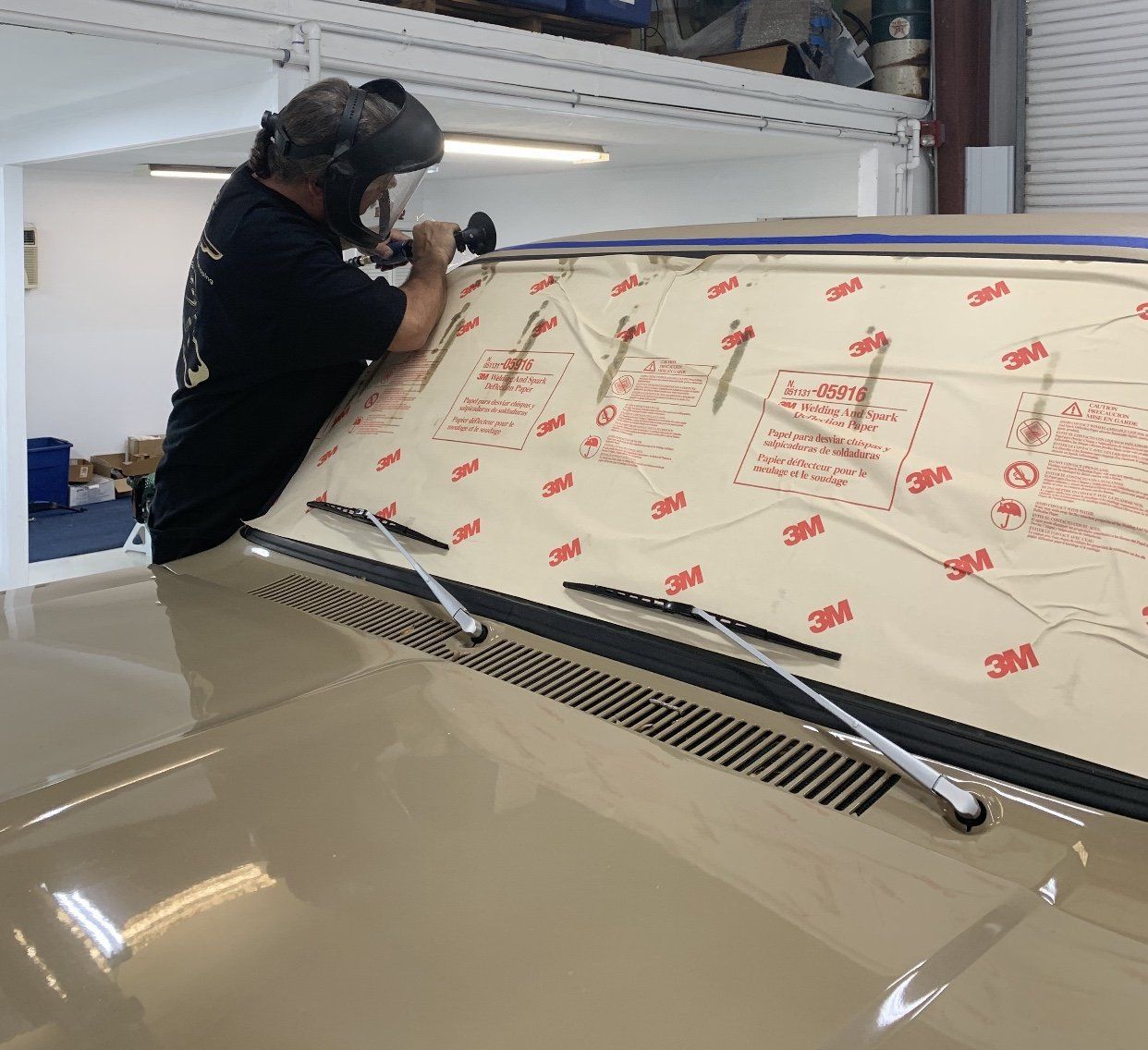 Person working on a car windshield wrapped in protective film inside a garage