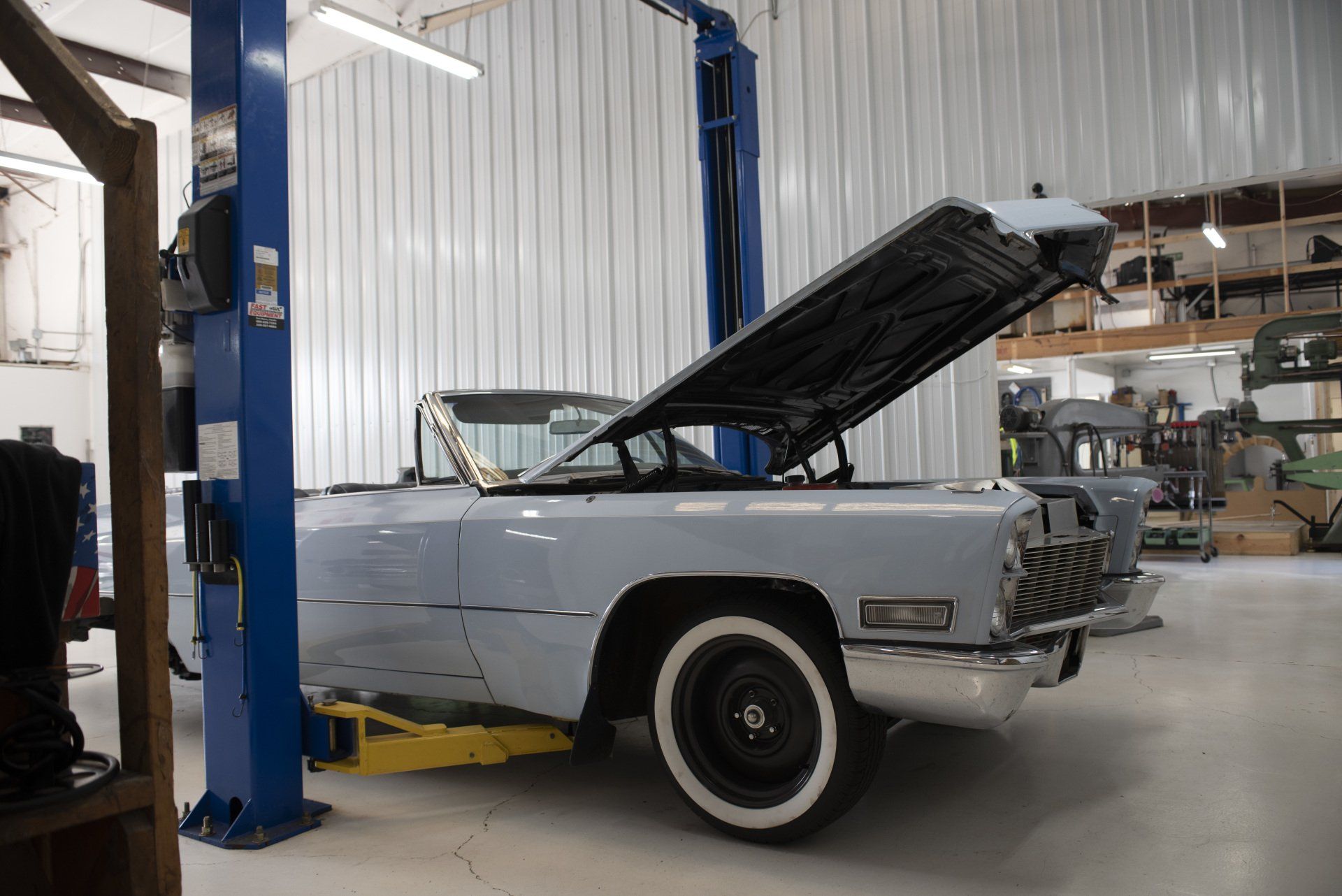 Classic light blue convertible on a lift in an auto shop, hood open for maintenance