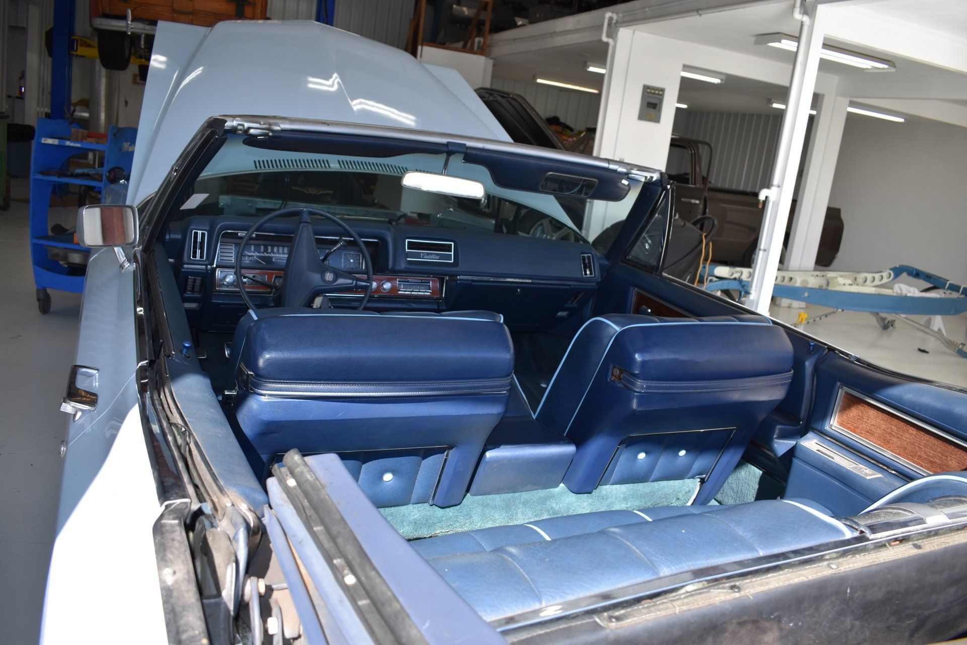Blue convertible car with its top down in a garage, front hood open and interior exposed