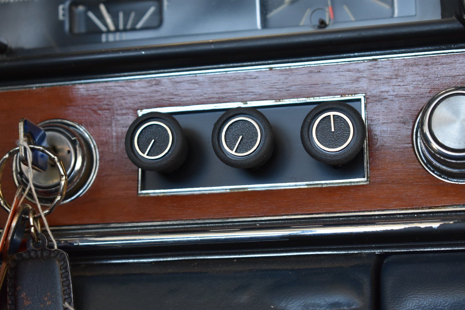 Car dashboard with wood trim and three round black climate control knobs
