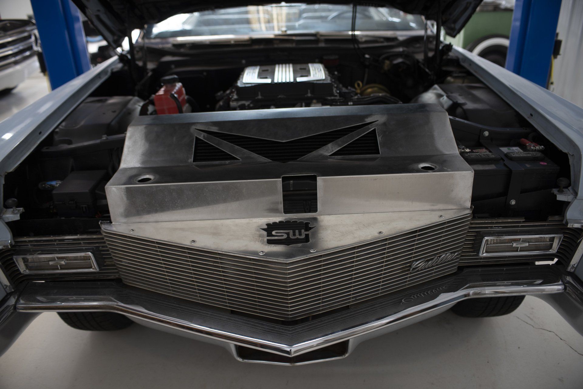 Black sports car rear with open engine cover in a garage, showing custom mesh grille and center exhaust