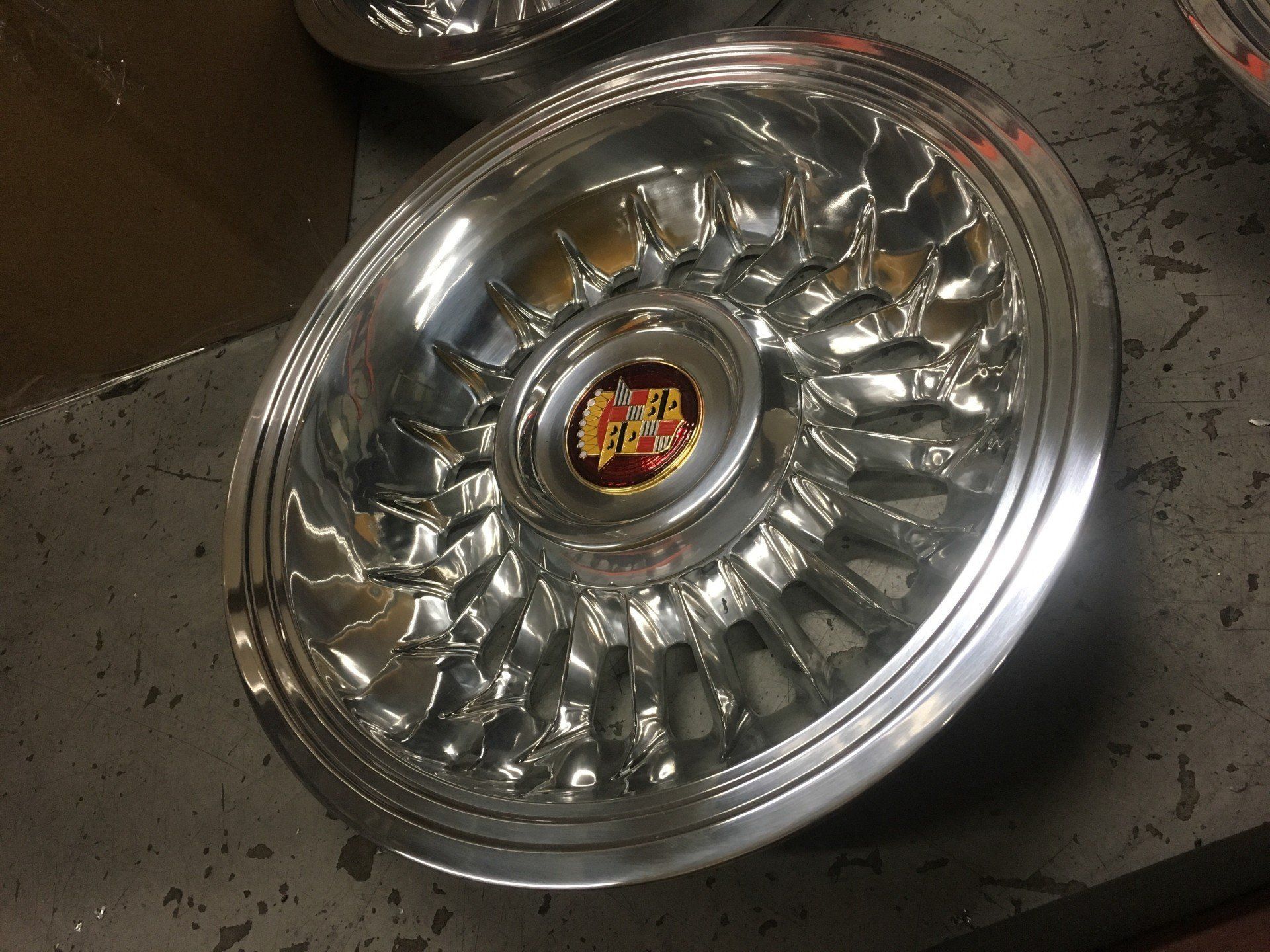 Chrome alloy wheel rim with reflective spokes and a center logo, lying on a floor.