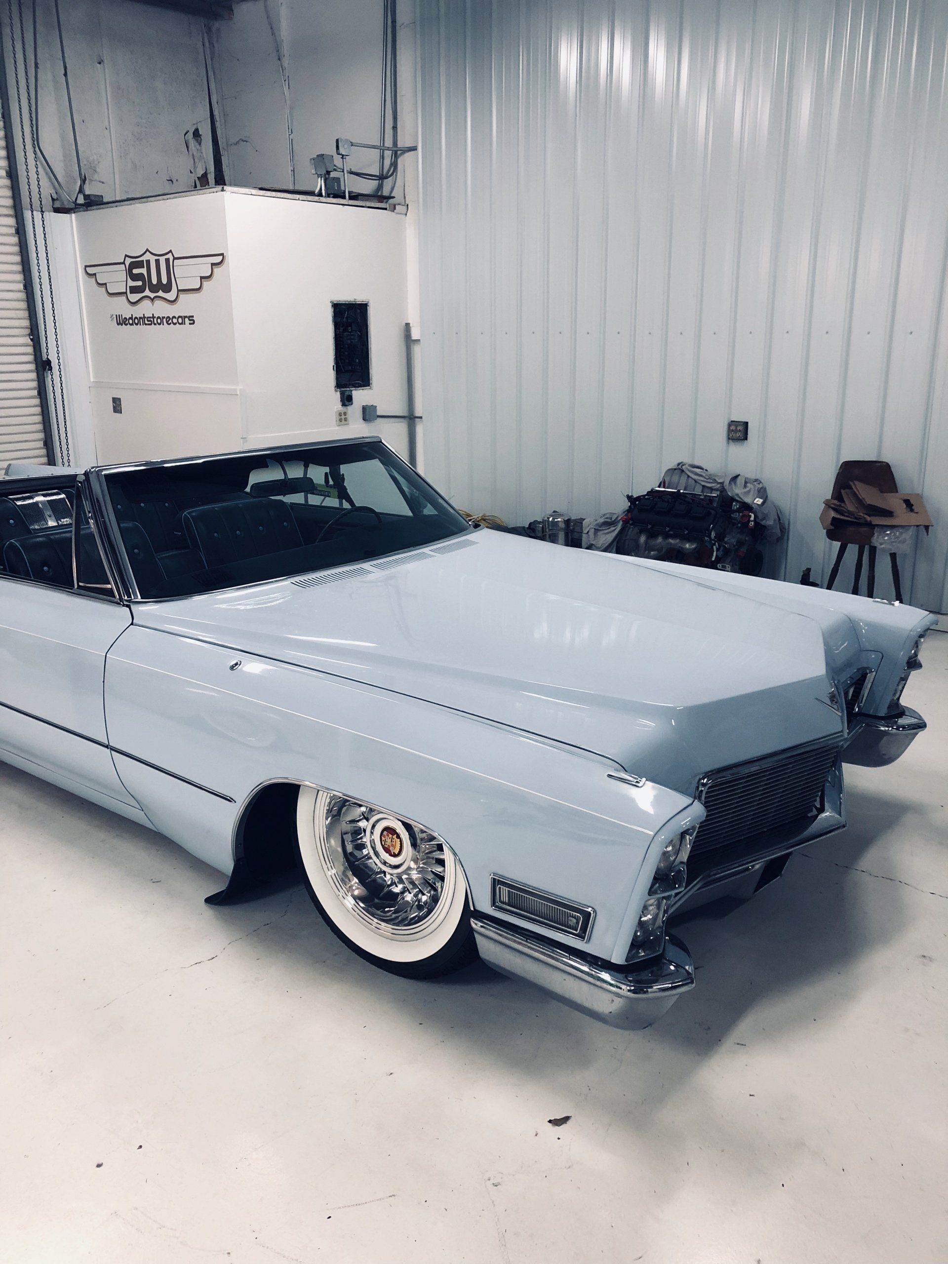 Classic white lowrider car in a garage, with chrome grille and whitewall tires.