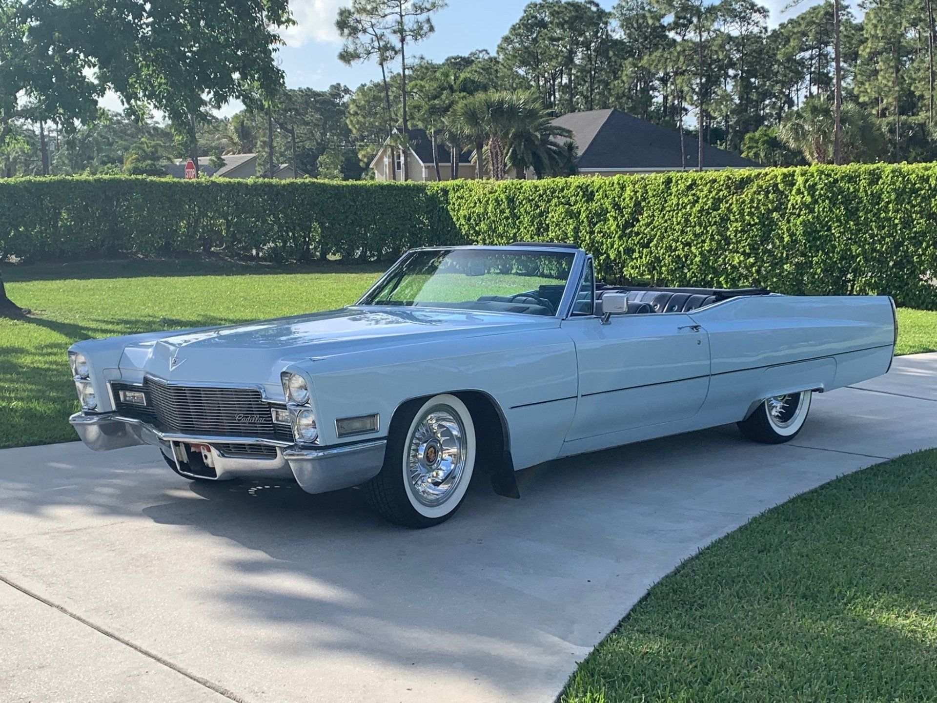 Light blue vintage convertible parked on a driveway with green lawns and trees behind it
