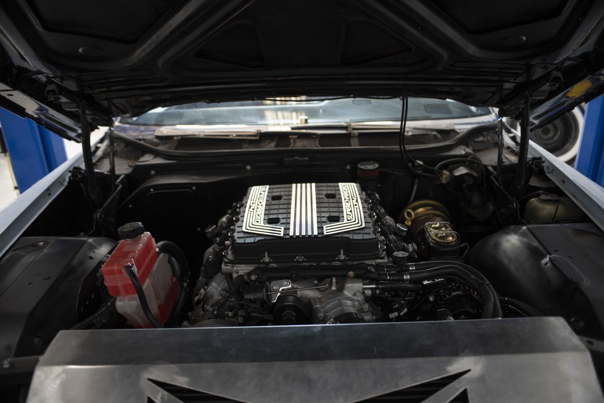 Car engine bay with hood open, showing a central engine and visible red battery on the left
