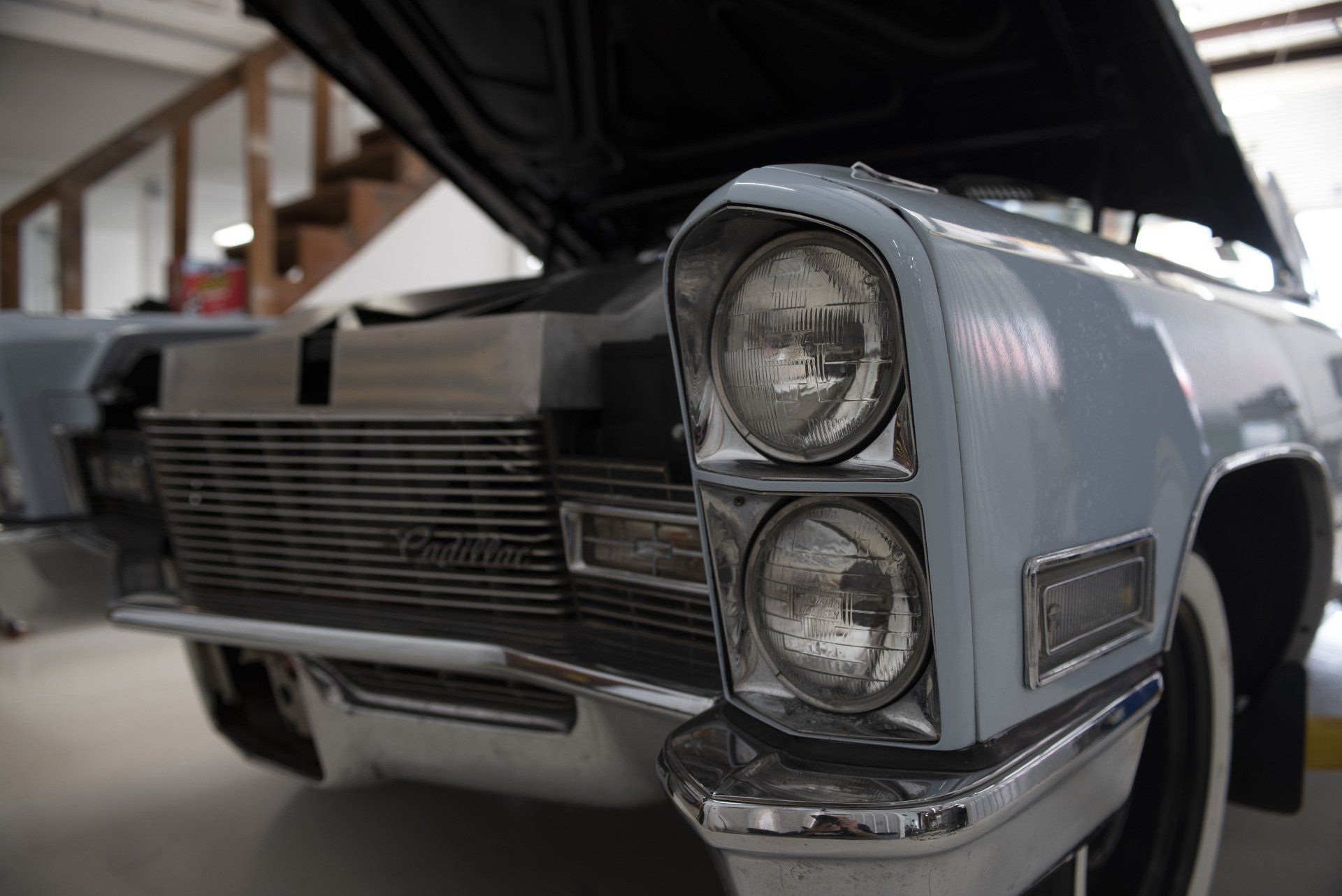Close-up of a classic silver car with open hood and twin headlights indoors