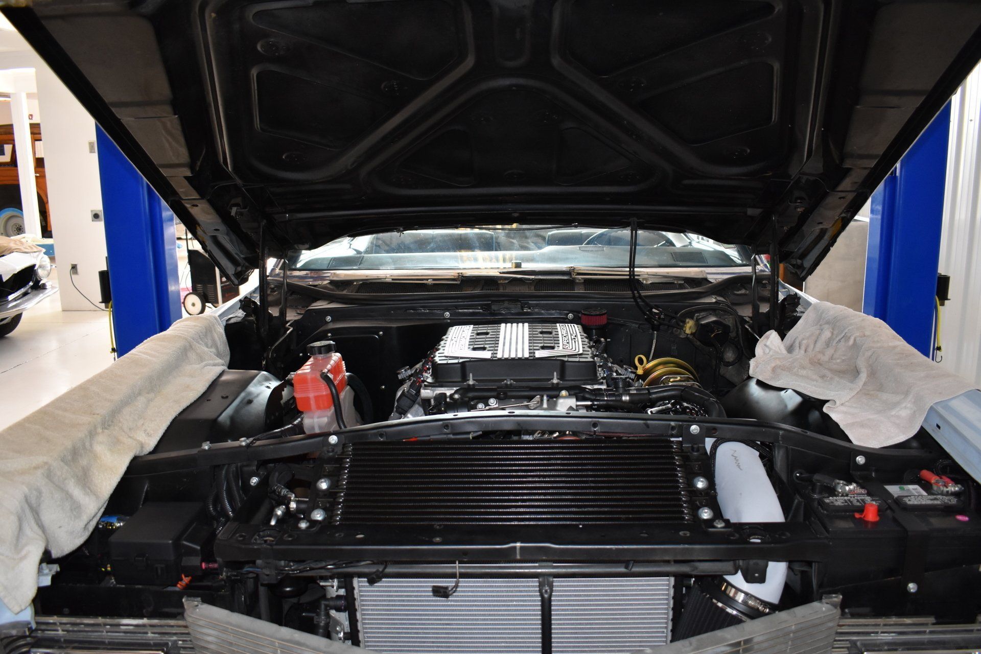 Car engine bay with hood open, showing radiator and components in a garage repair bay