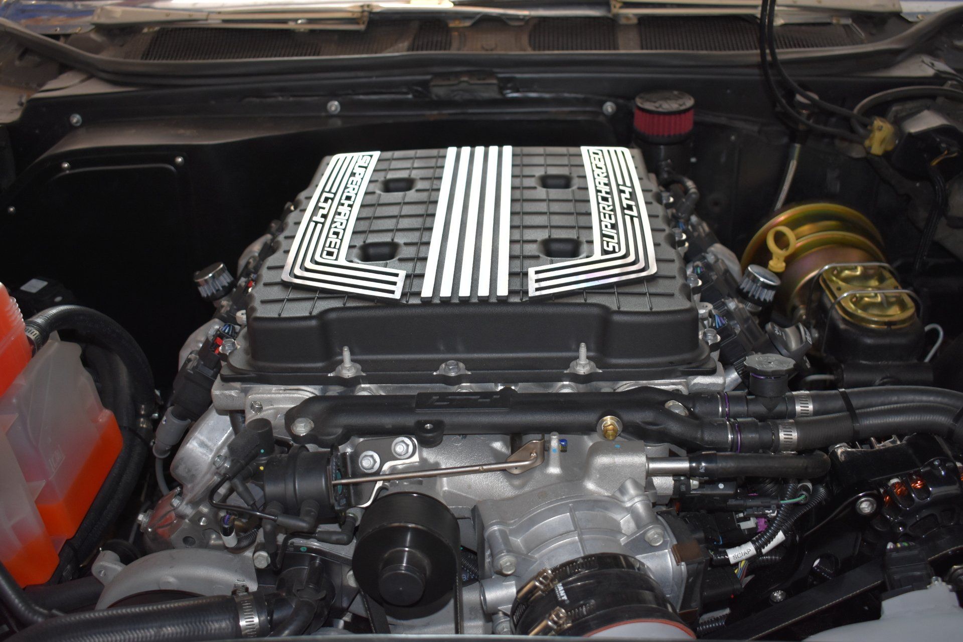 Car engine bay with a large black-and-silver striped engine cover and visible hoses and components