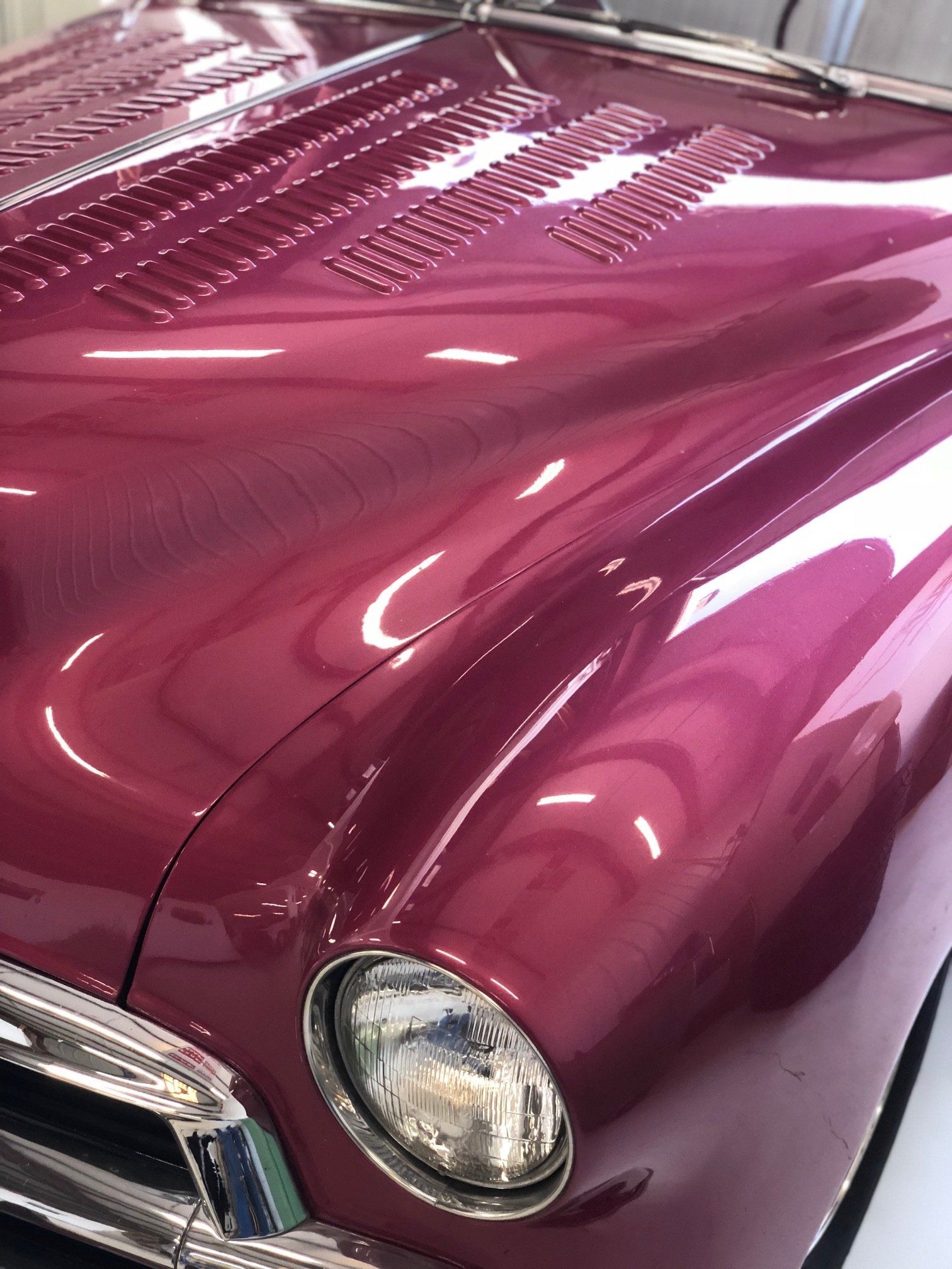 Close-up of a glossy magenta vintage car hood and front headlight indoors