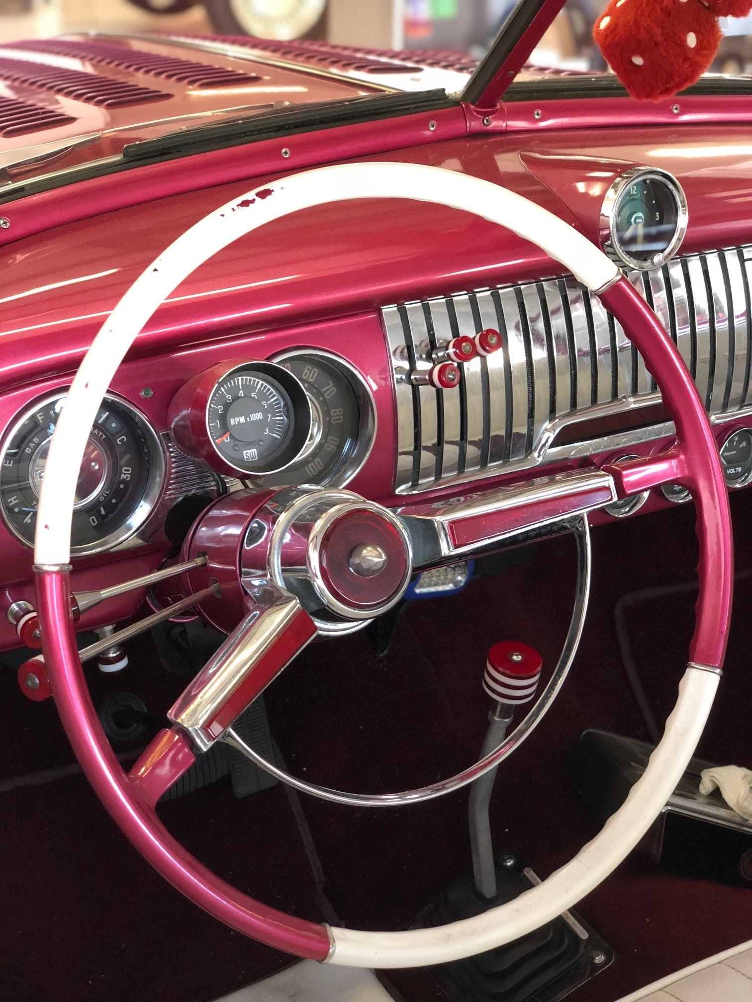 Pink and white steering wheel and chrome dashboard of a vintage car interior