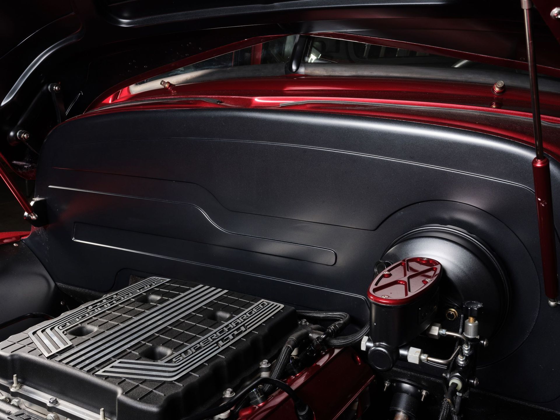Custom car engine bay with black paneling, red accents, and a polished intake component