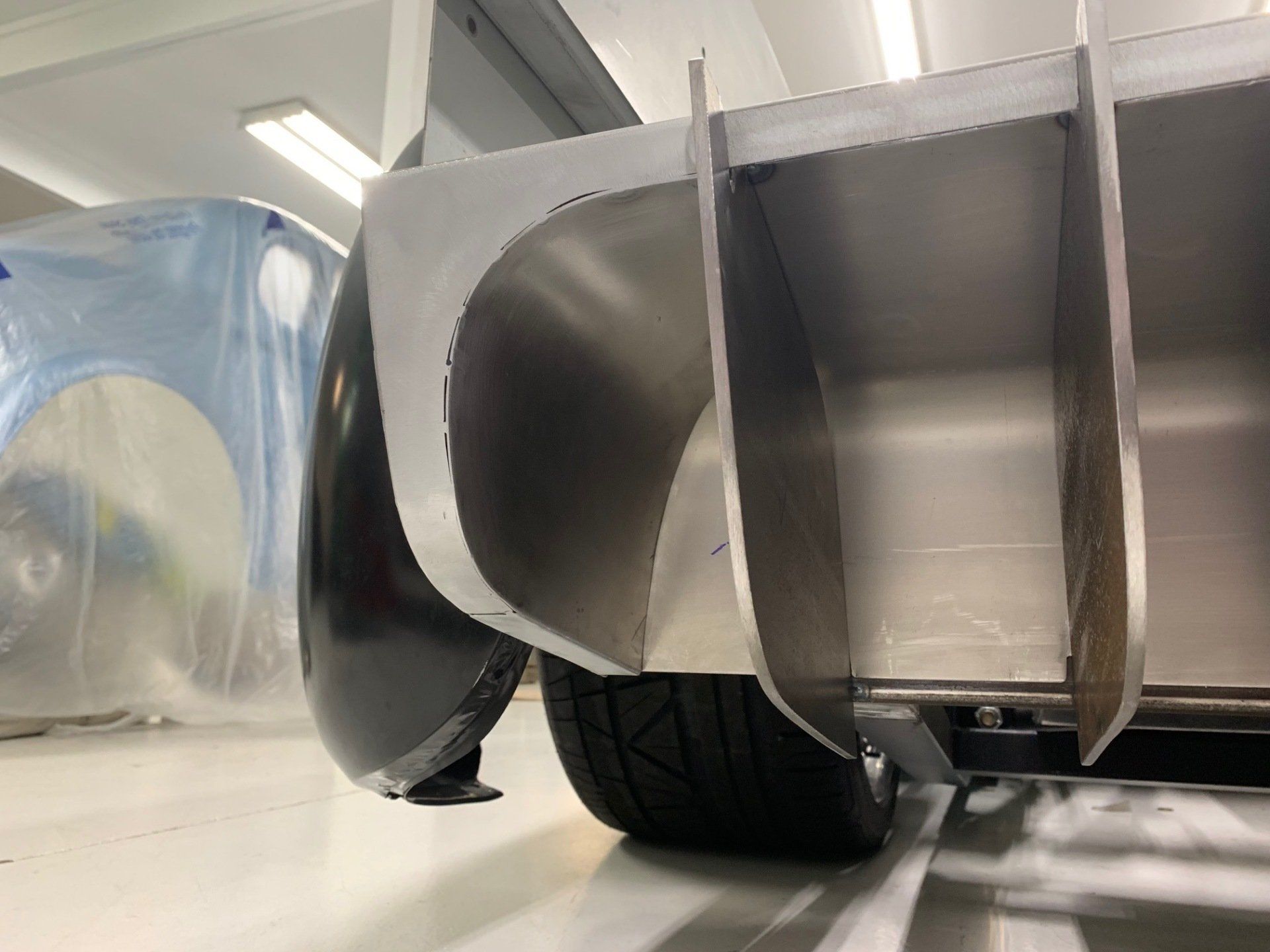 Close-up of a car’s rear diffuser with a tire in a garage, parts covered in protective plastic