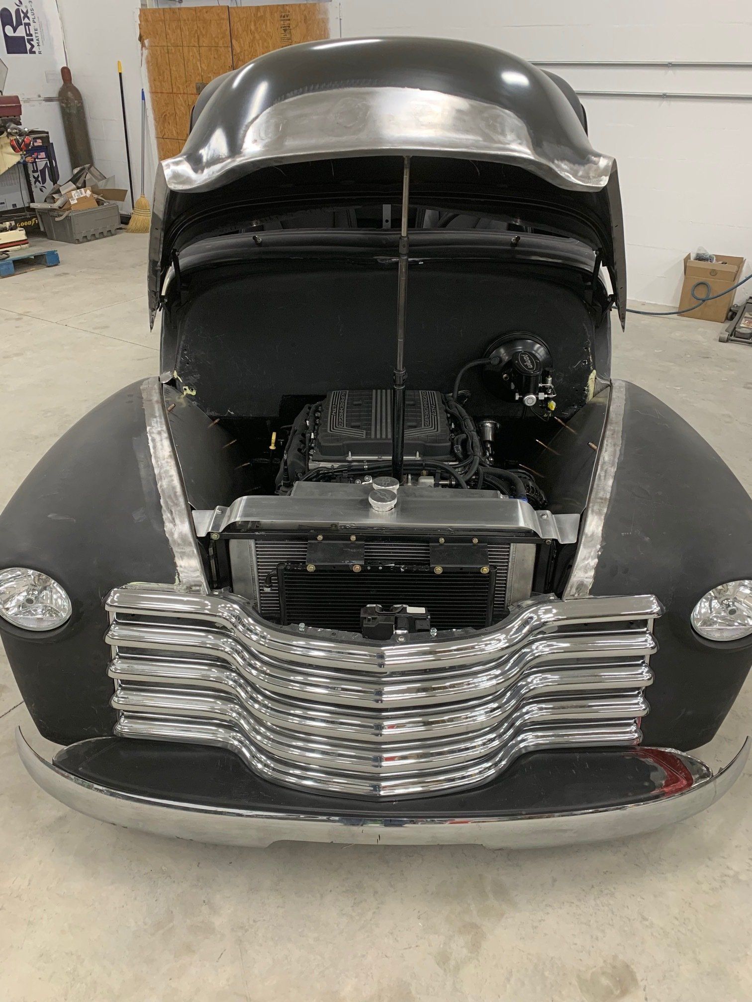 Front view of a black vintage car with hood open, showing engine and chrome grille in a garage