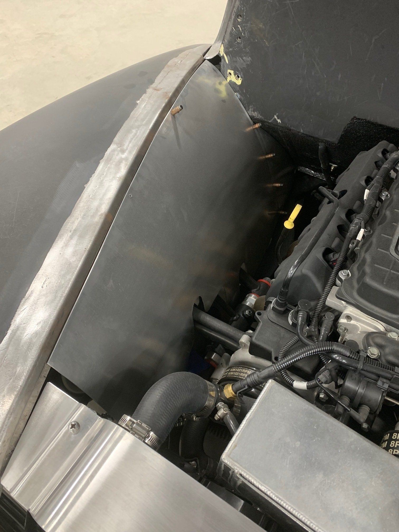 Car engine bay with silver body panels and a black interior compartment showing hoses and wiring