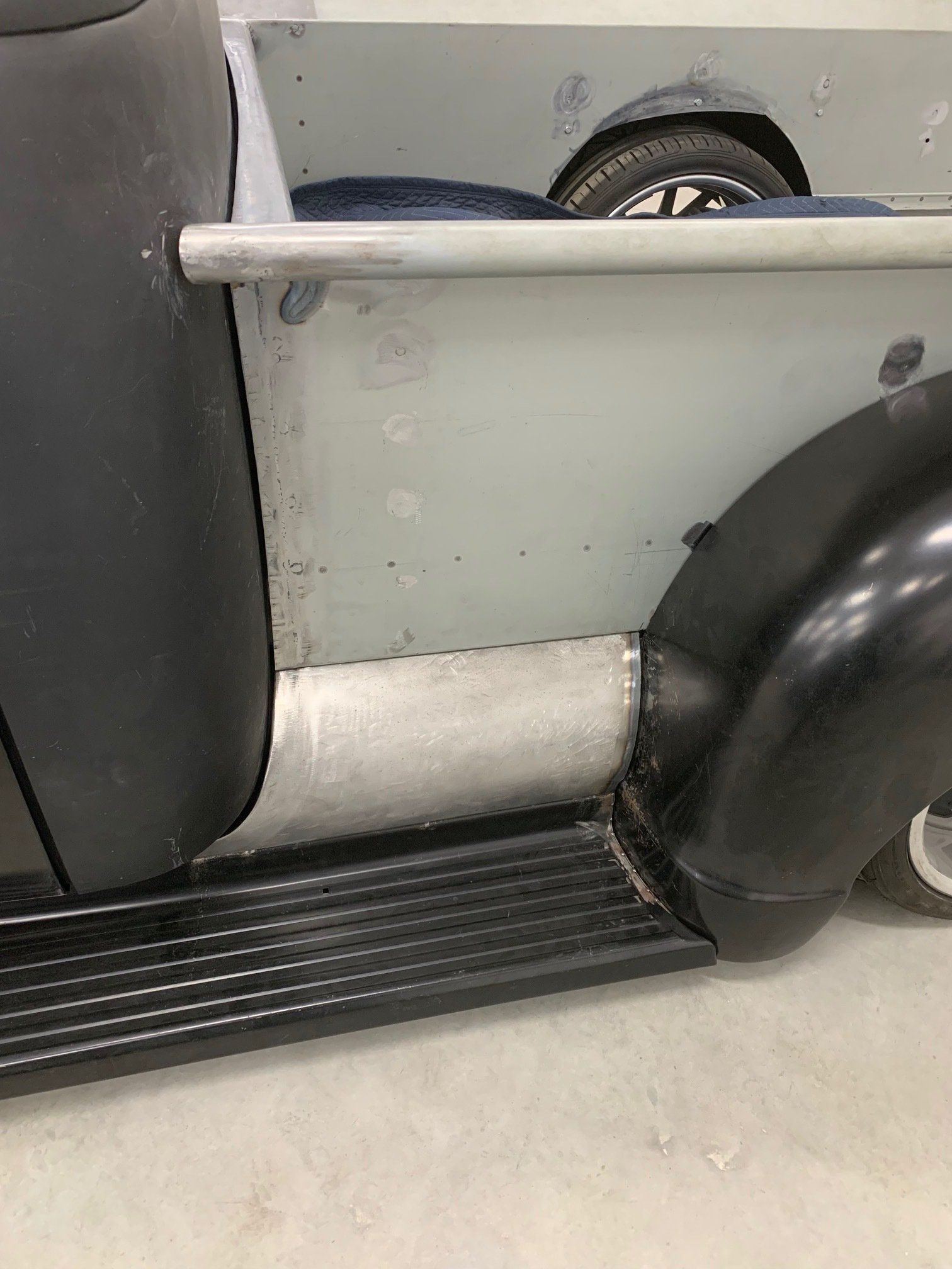 Close-up of a black and white vintage car side panel and running board inside a garage