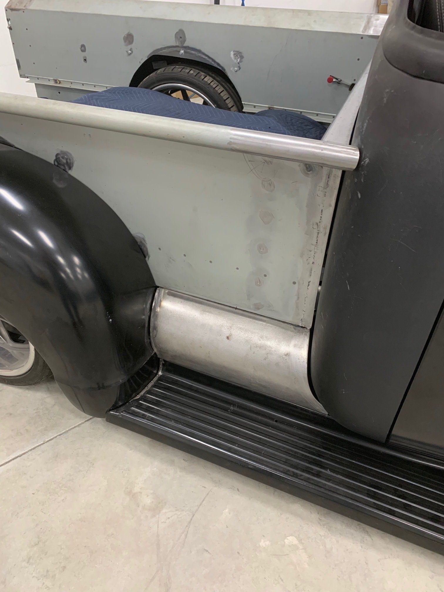 Close-up of a vintage vehicle’s side step, rear wheel, and silver body panel in a garage.