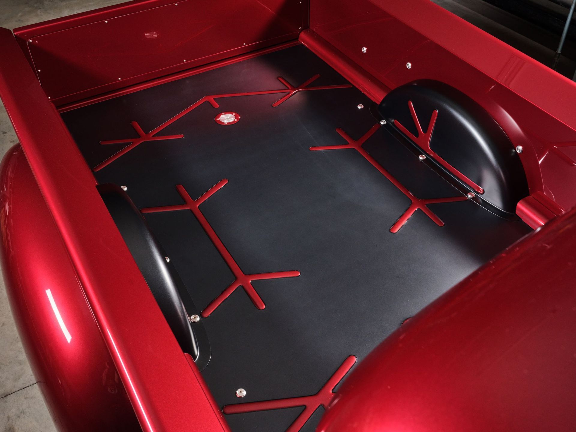 Red car trunk with black custom lining and red straps holding a spare wheel well cover