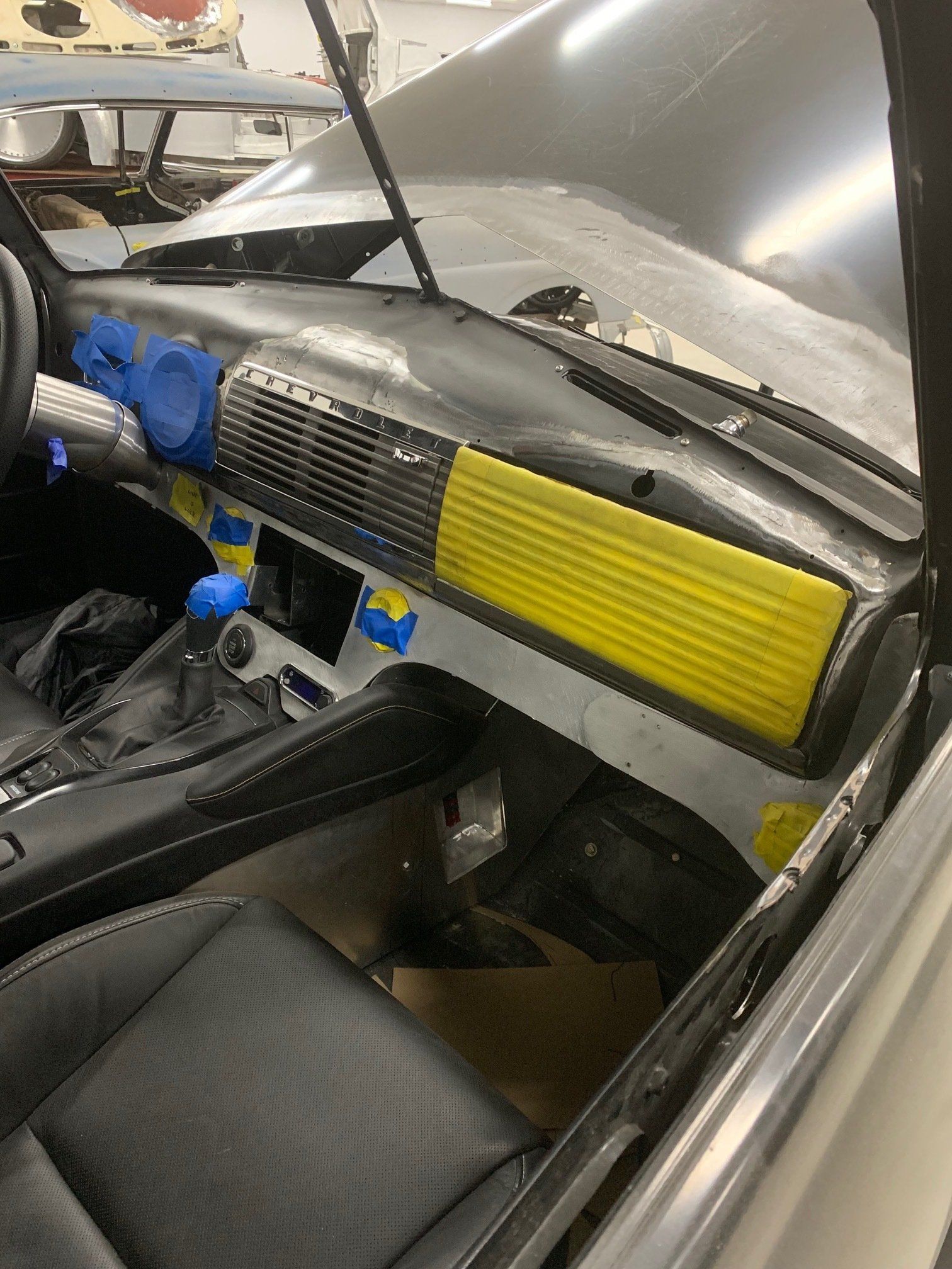 Car interior with dashboard removed, yellow vent panel, and exposed blue wiring during repair