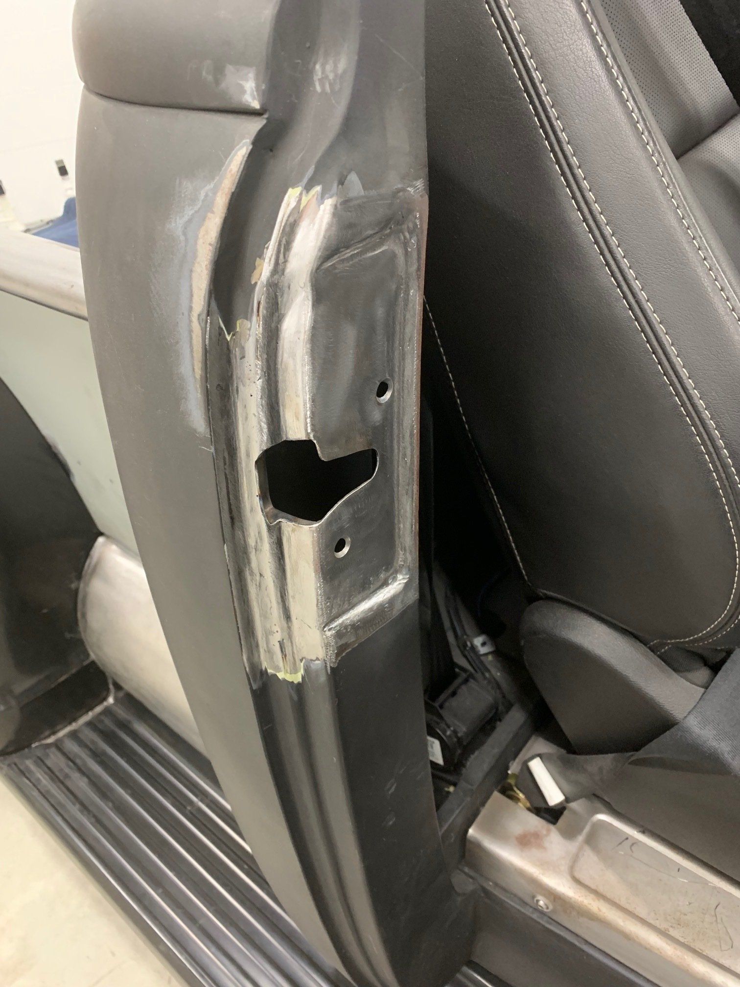 Damaged car door pillar with exposed metal near the front seat and floor mat