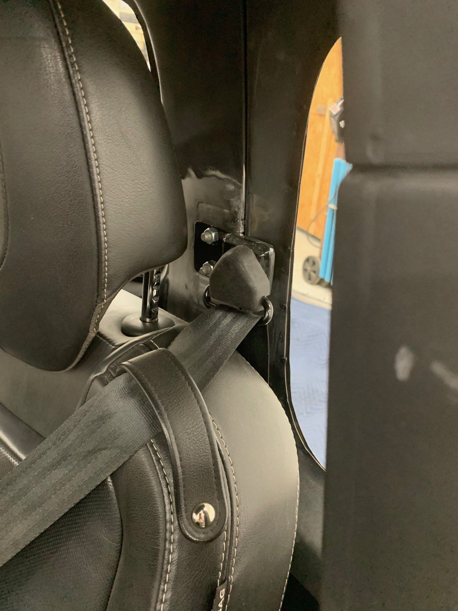 Black leather car seat with a seat belt strap and headrest visible in the back seat area