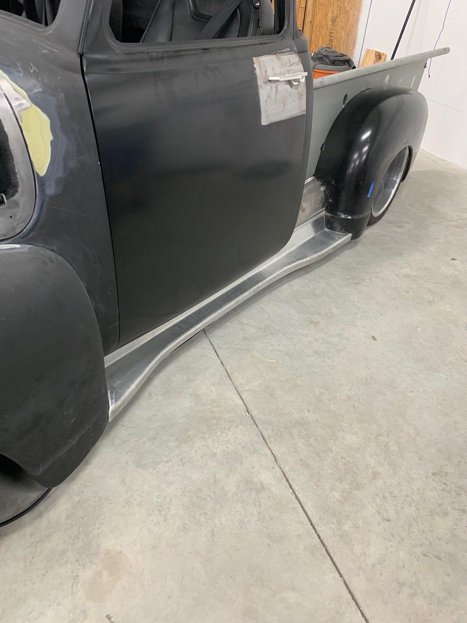 Black vintage car side panel with curved silver rocker trim in a garage, close-up view