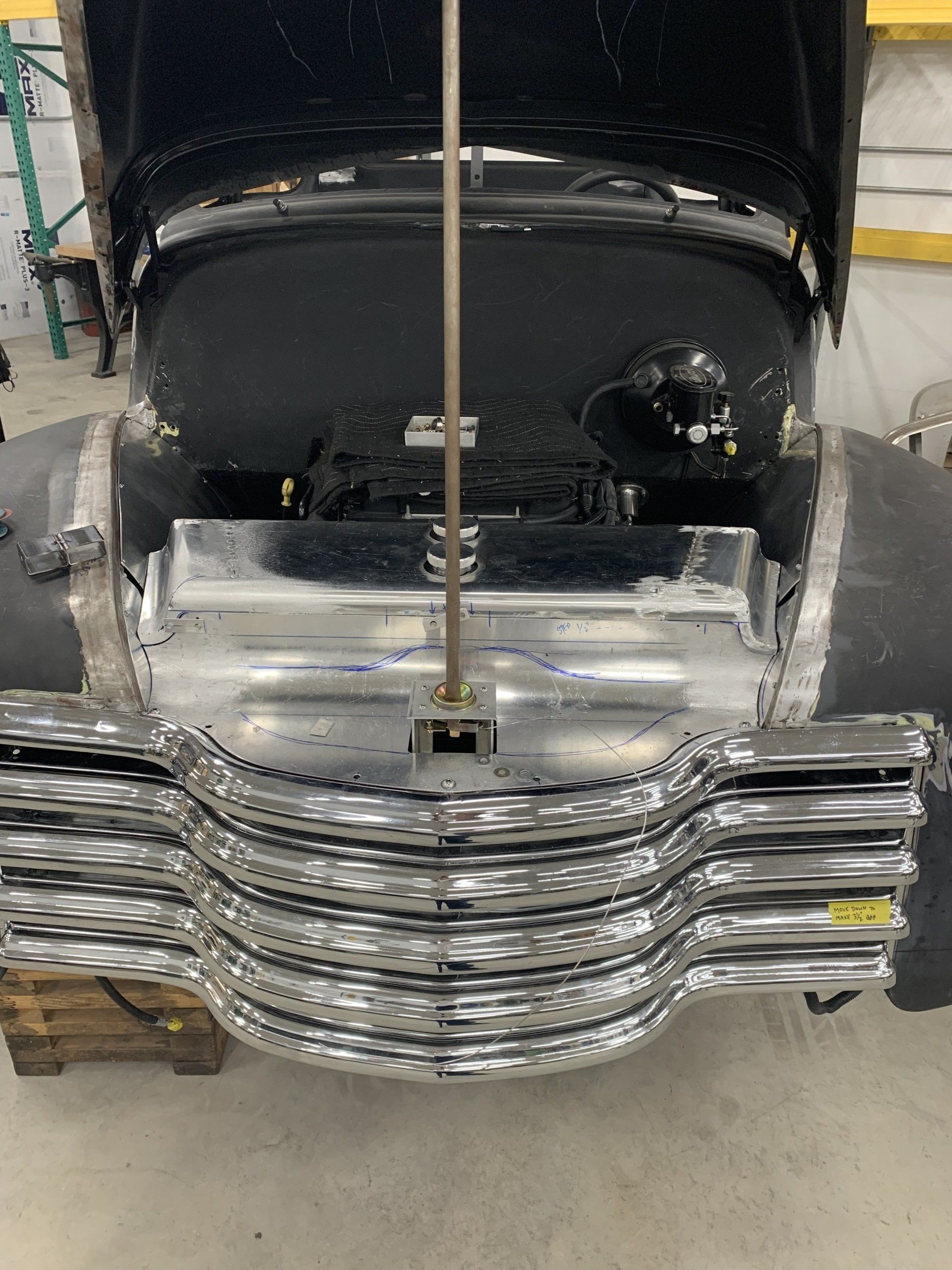 Front view of a vintage black truck with a chrome grille in a garage, hood open.