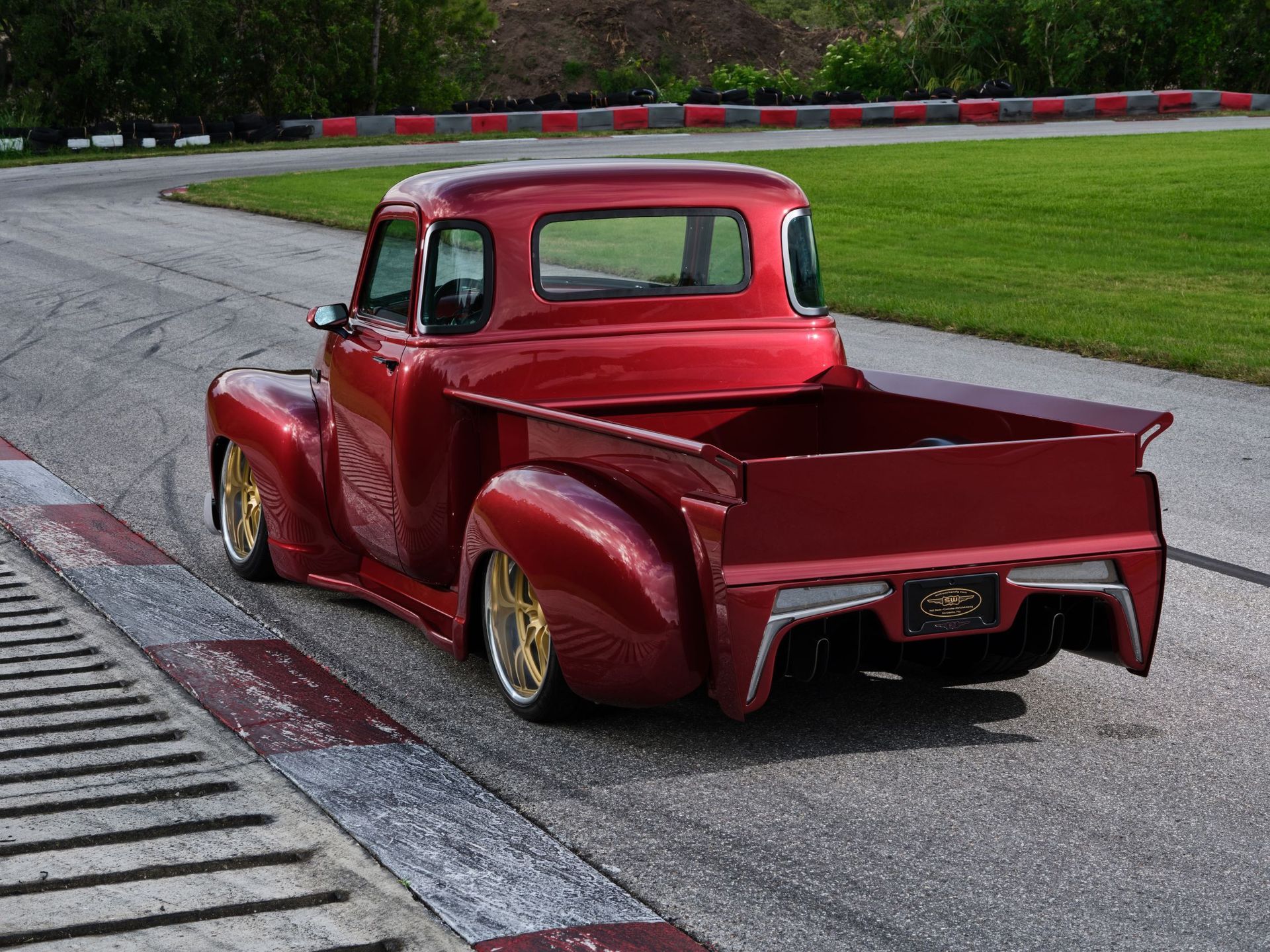 Red vintage pickup truck on a racetrack curve, seen from the rear.