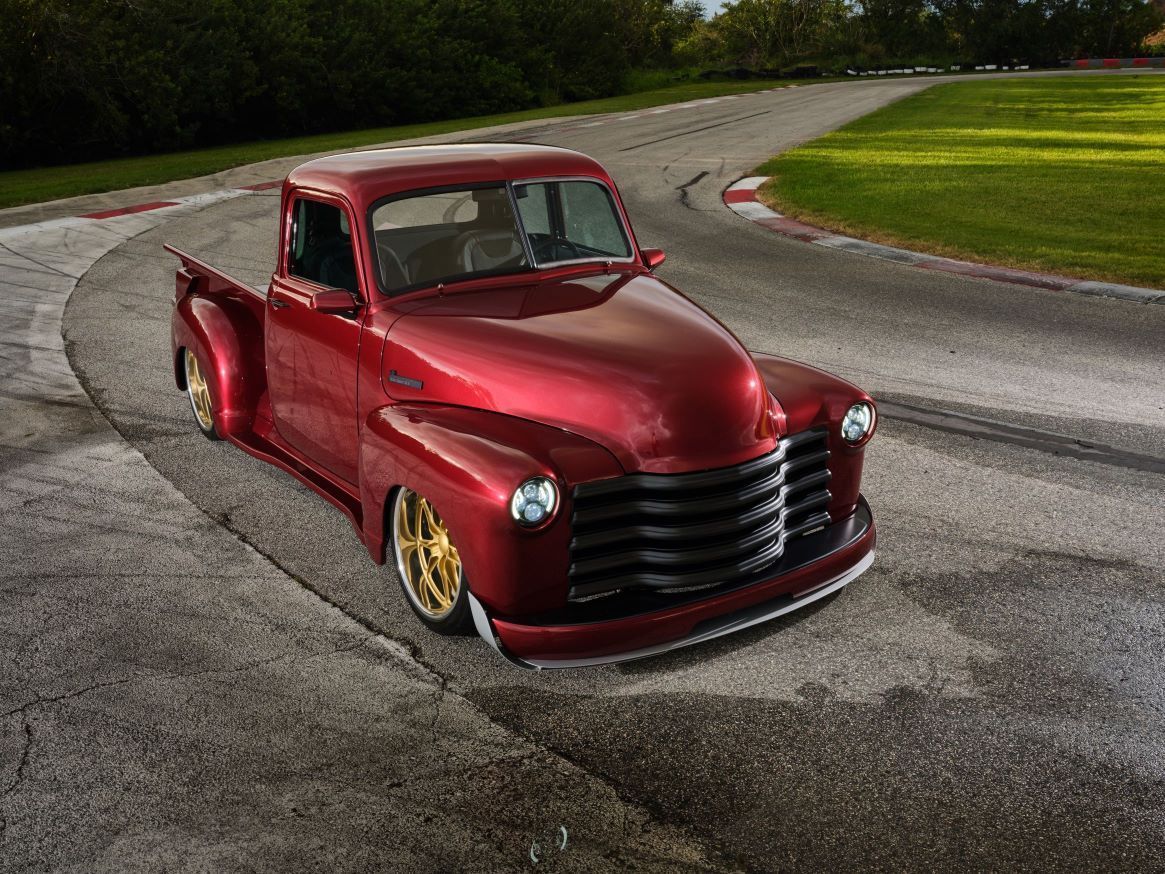 Red vintage pickup truck on a curving road with grass and trees